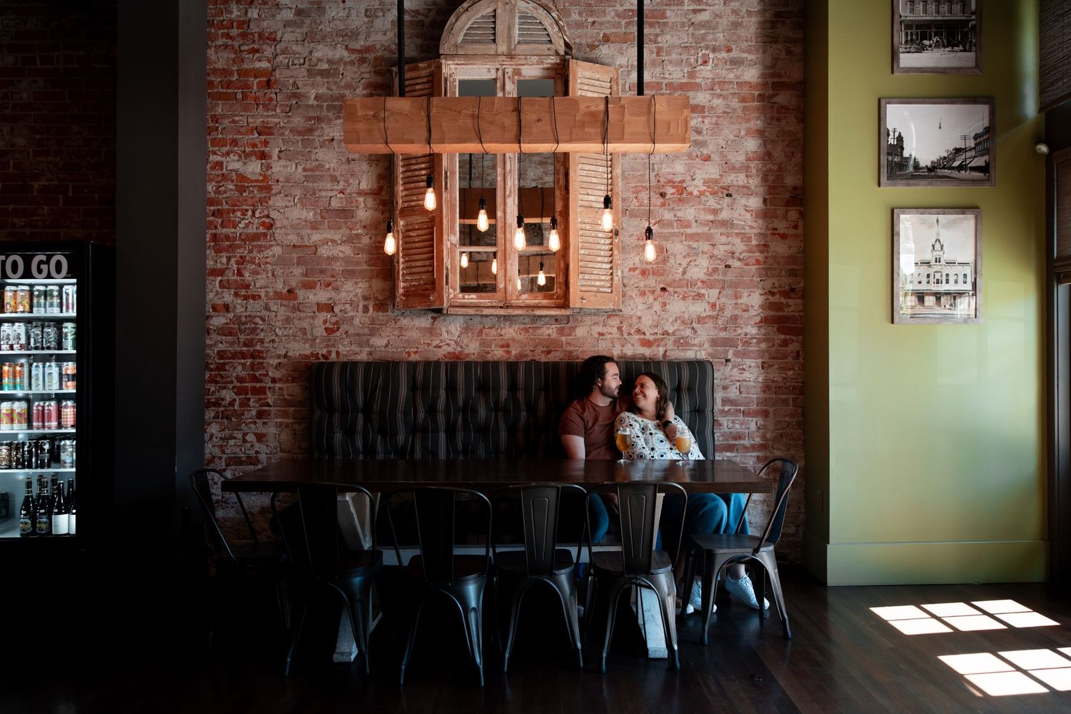 Two people sit at a table in a rustic coffee shop with exposed brick walls and industrial metal chairs.
