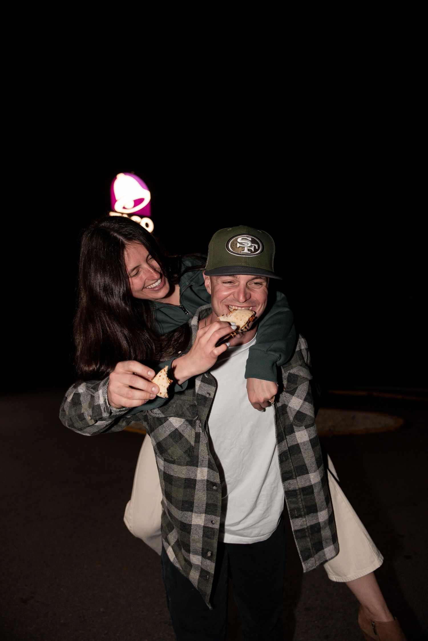 Two people in plaid flannel and casual wear share a playful moment together in a dark setting.