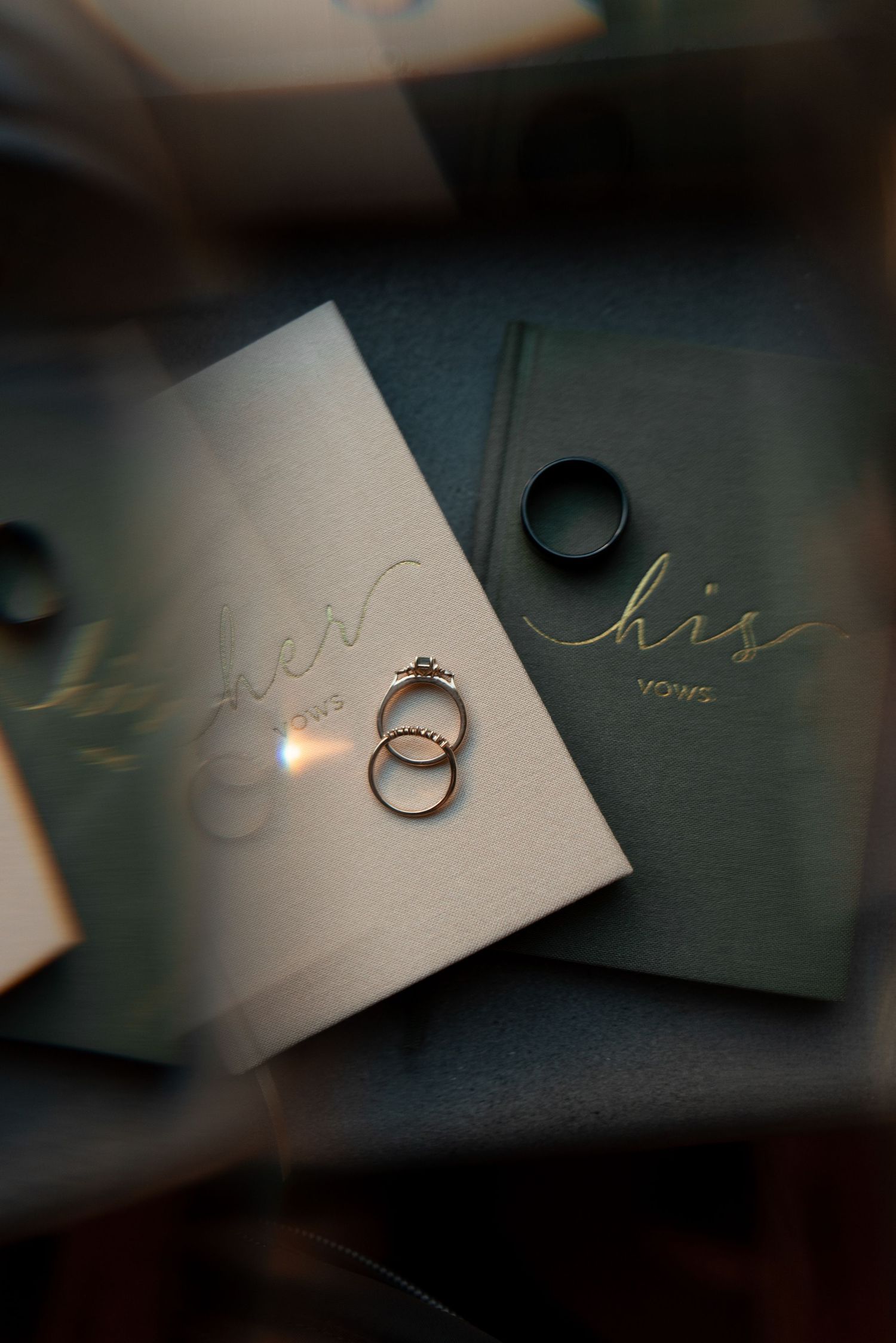 Wedding rings cast dramatic shadows on elegant his and hers cards in moody lighting creating an artistic composition.