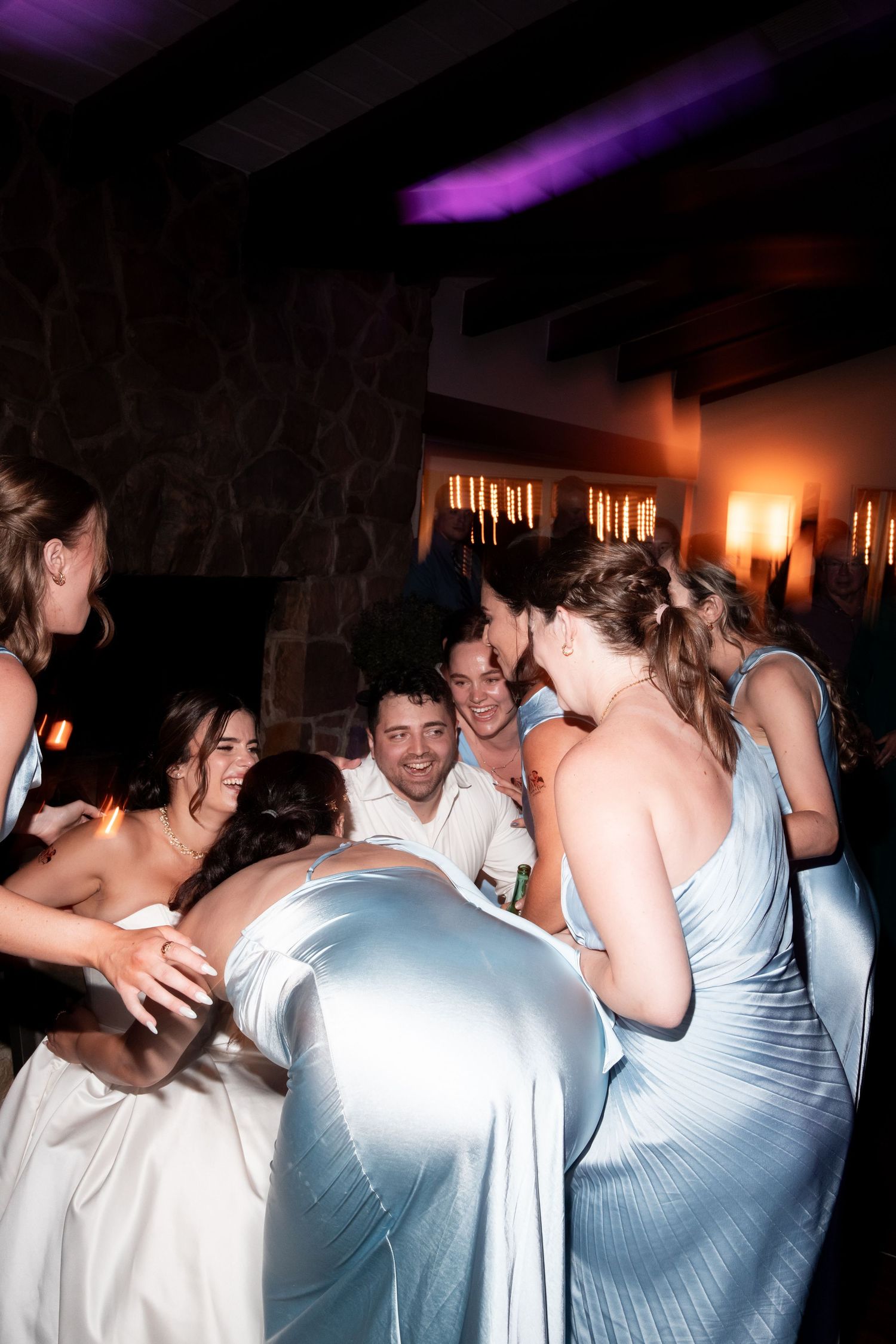 Wedding guests dancing and celebrating together at a reception with purple lighting and festive atmosphere.