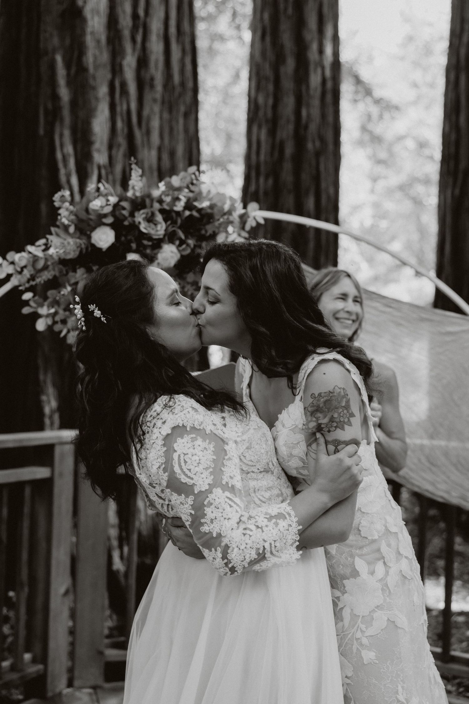 A romantic black and white wedding photo series showing two brides sharing joyful moments together in a forest setting.