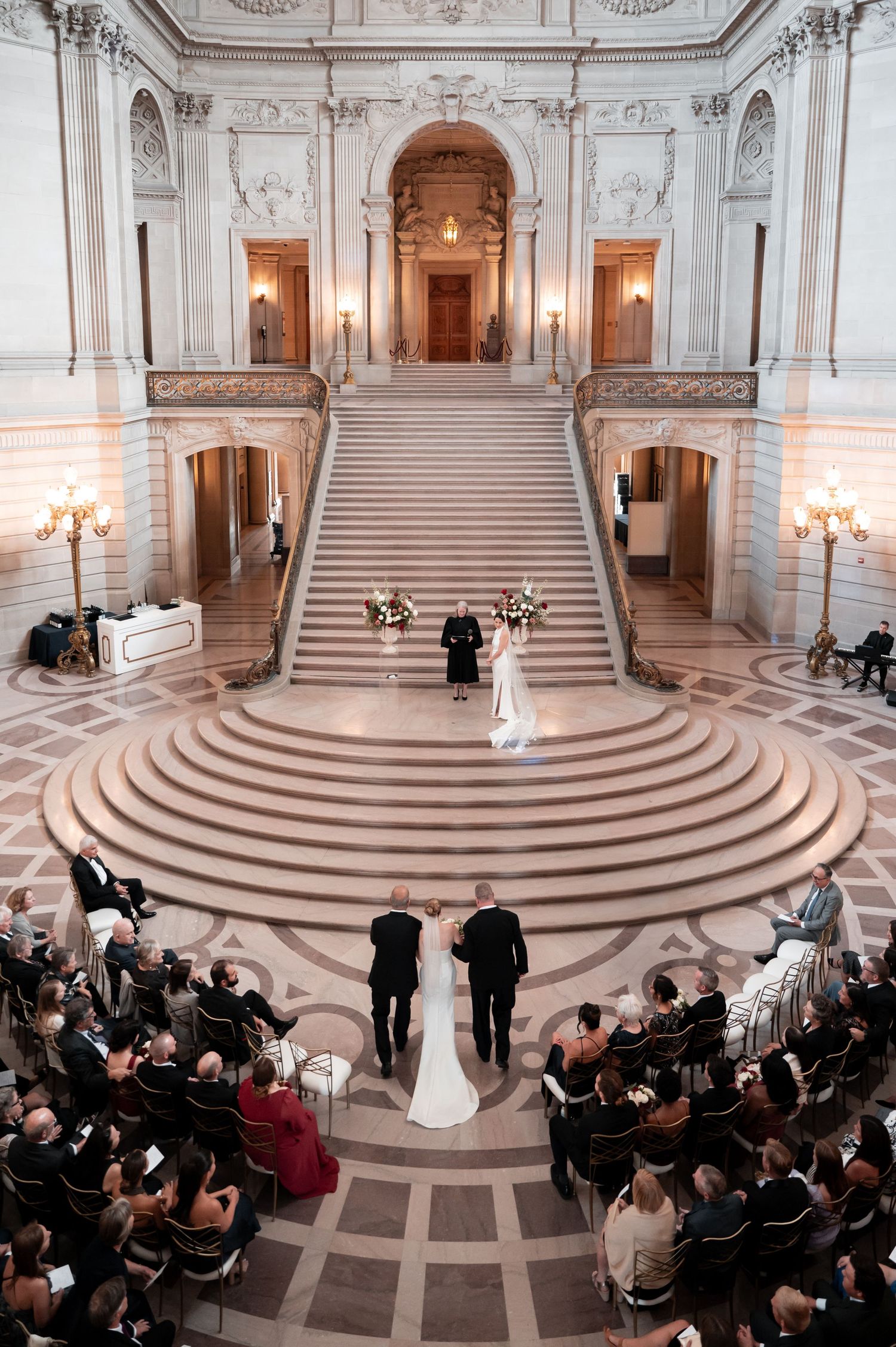 Elegant wedding ceremony at San Francisco City Hall grand staircase with guests seated in circular rotunda.