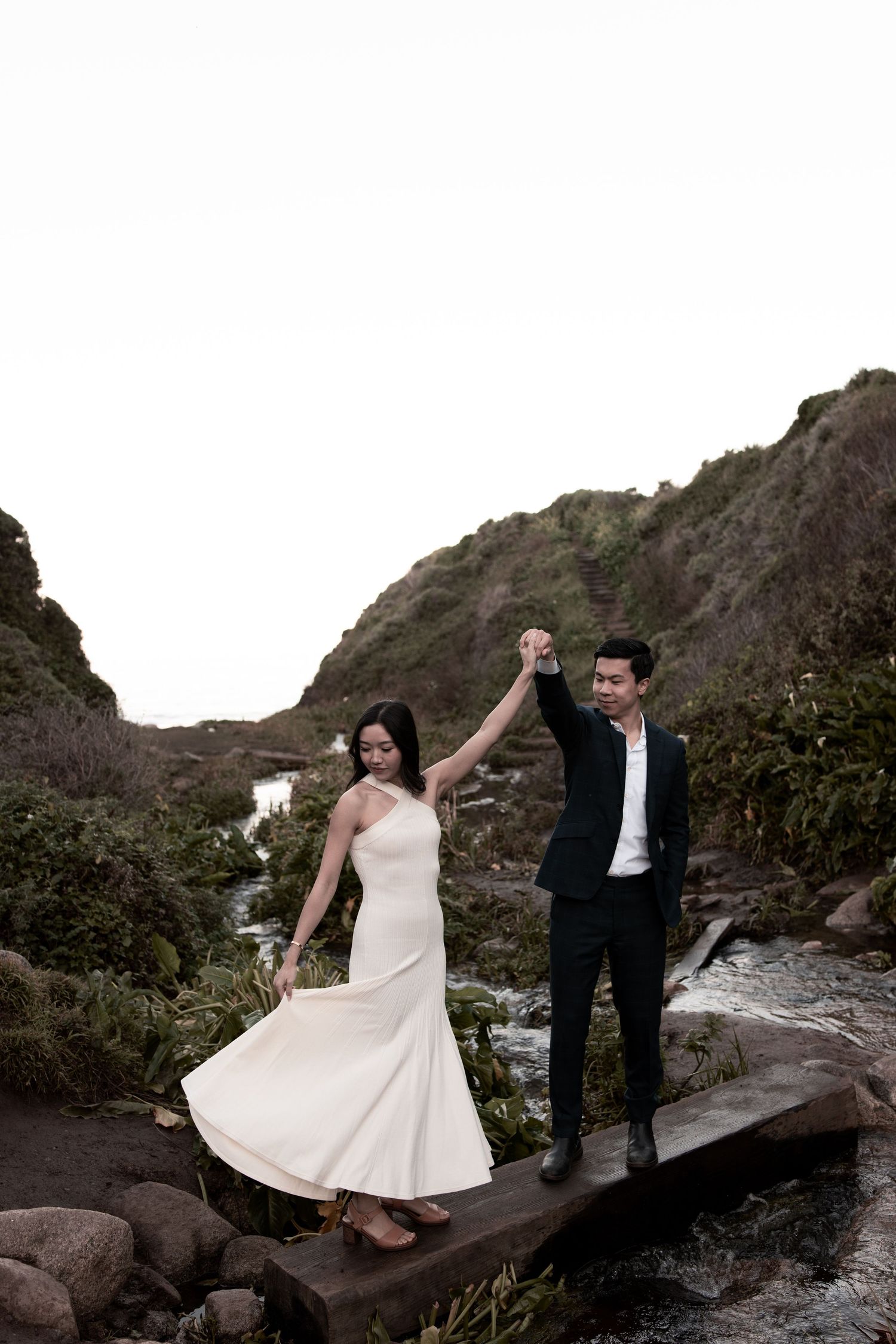 A couple in wedding attire poses together on rocky coastal cliffs during a romantic outdoor photo session.