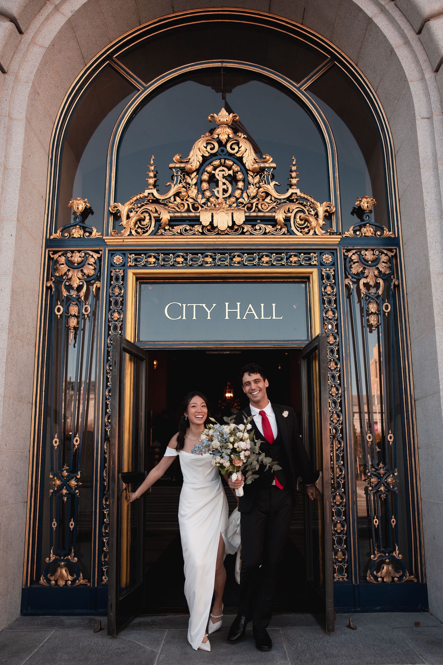 Elegant couple exits through ornate gold-trimmed doors at San Francisco City Hall during their wedding celebration.