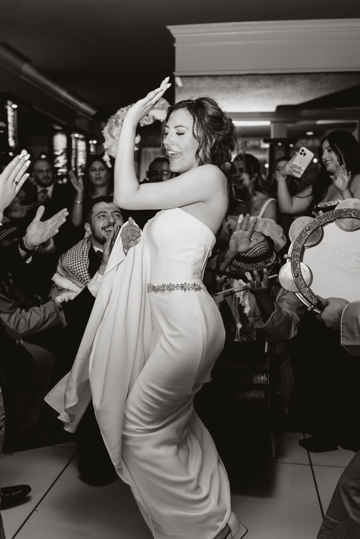 Black and white photo of a bride in a fitted white dress dancing joyfully at a wedding reception.