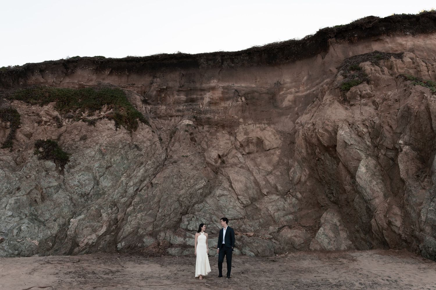 A series of panoramic photos showing a couple walking along a dramatic red rock cliff face in a desert landscape.