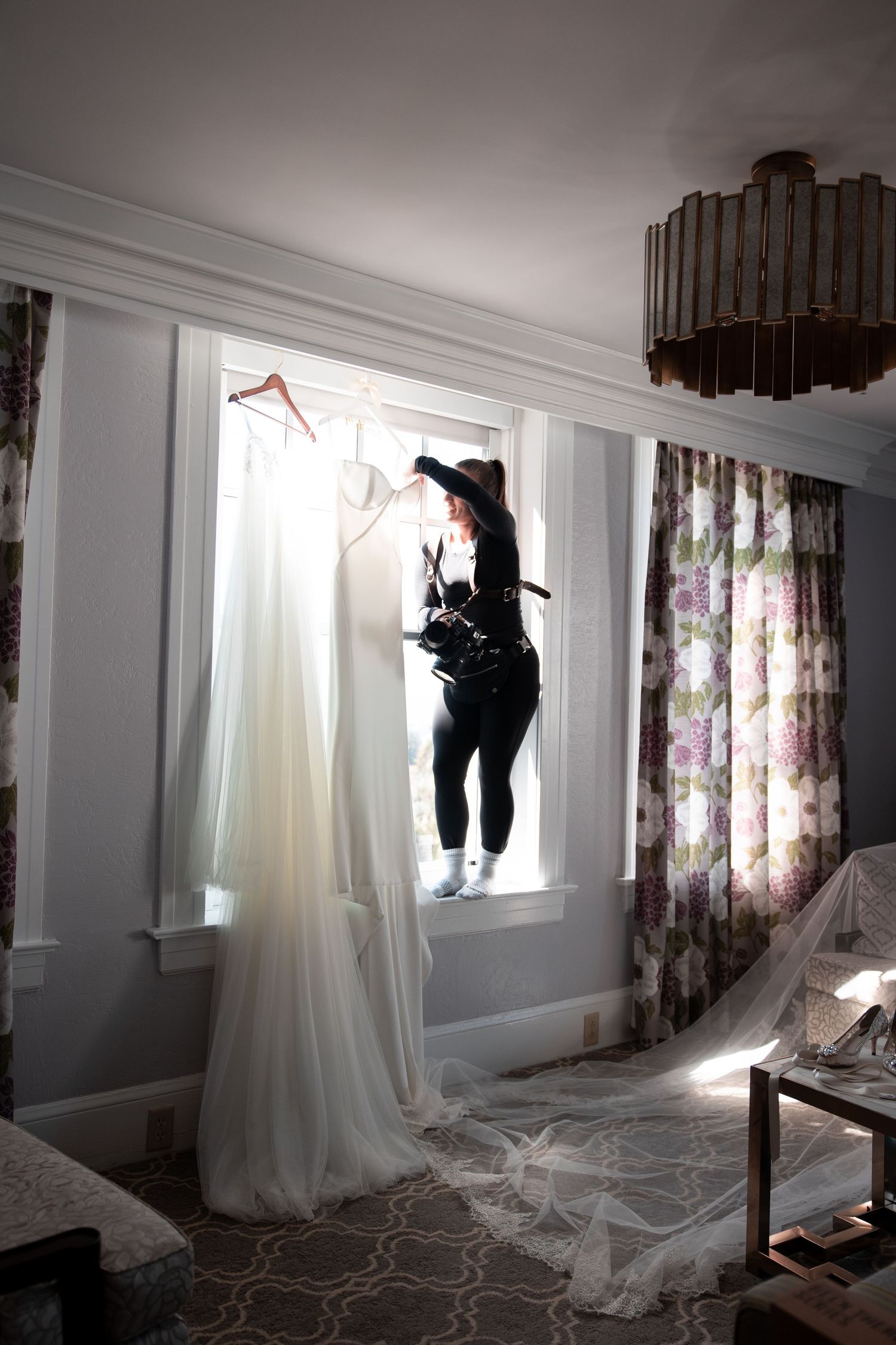 Silhouetted figure installing curtains in a bright room with floral drapes and white sheer panels.