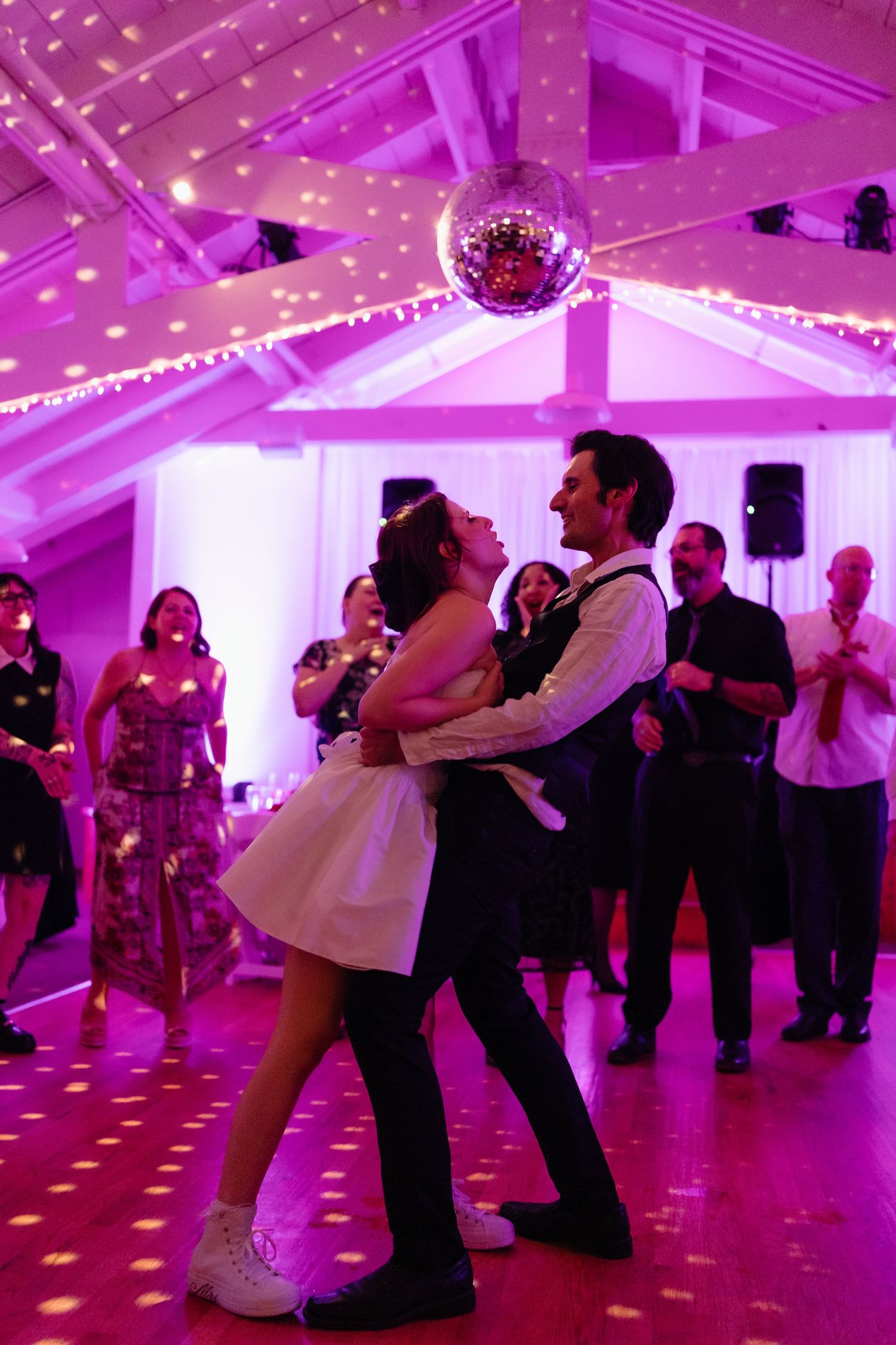 Couples dancing at a wedding reception under purple lighting and a disco ball creating a romantic atmosphere.