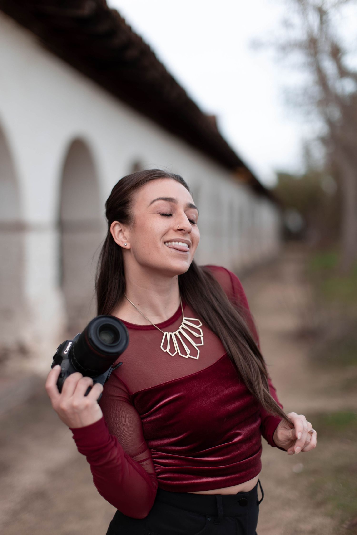 A person in a burgundy velvet top spins joyfully with arms outstretched in an outdoor setting.