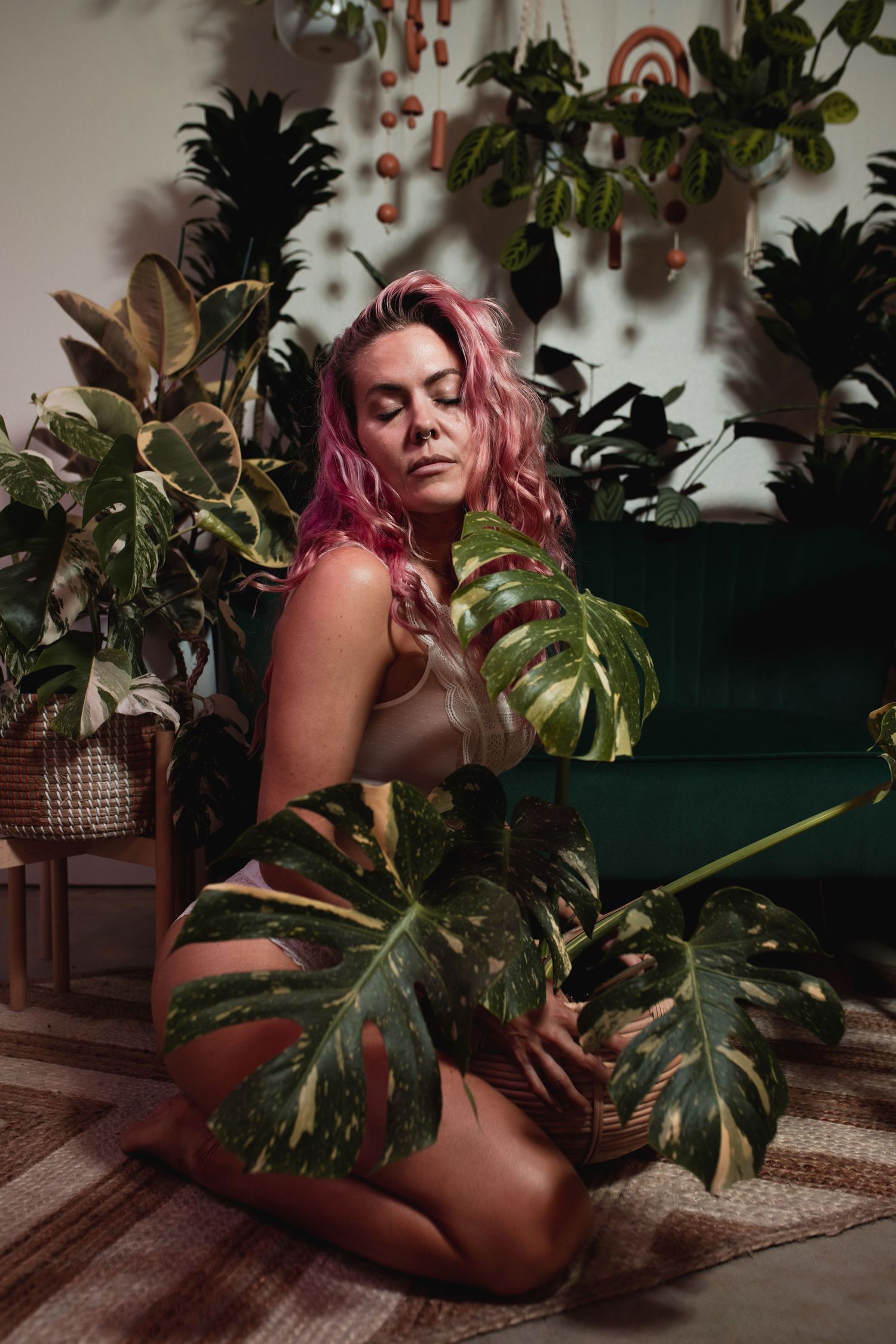 Artistic indoor photography with monstera leaves and houseplants against a green couch and decorative wall background.