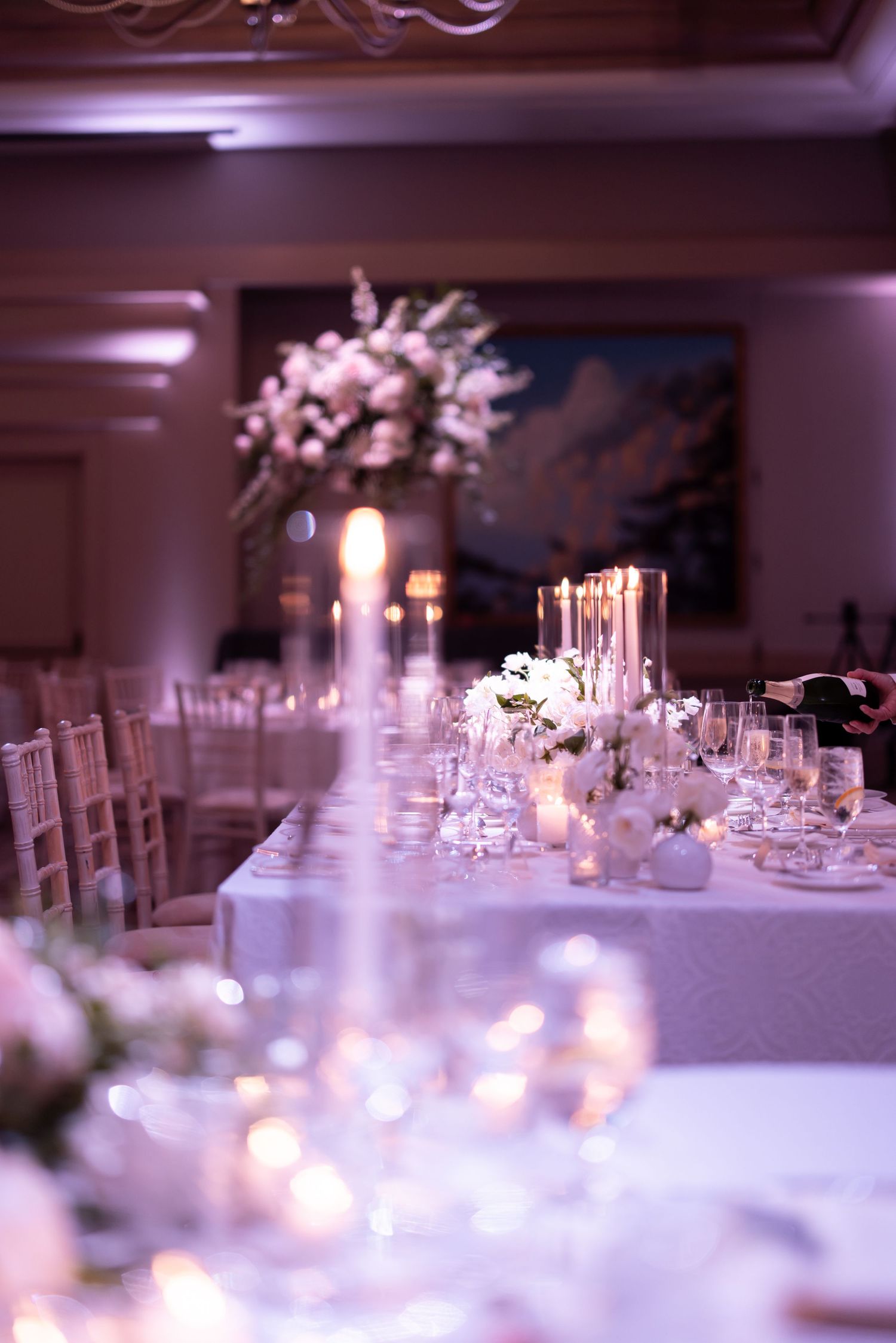 Elegant wedding reception table with white floral centerpieces, glowing candles, and crystal glassware in a softly lit ballroom.