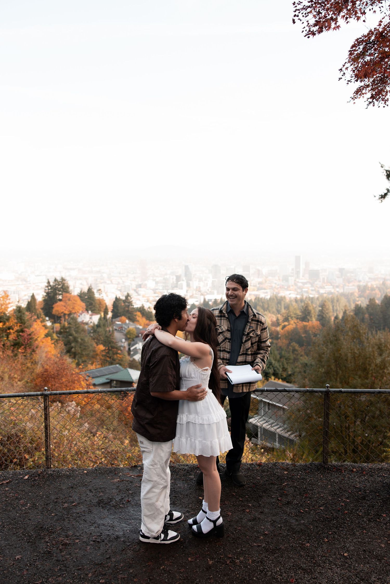 Three figures embrace while enjoying autumn views of Portland's skyline from a hilltop viewpoint at sunset.