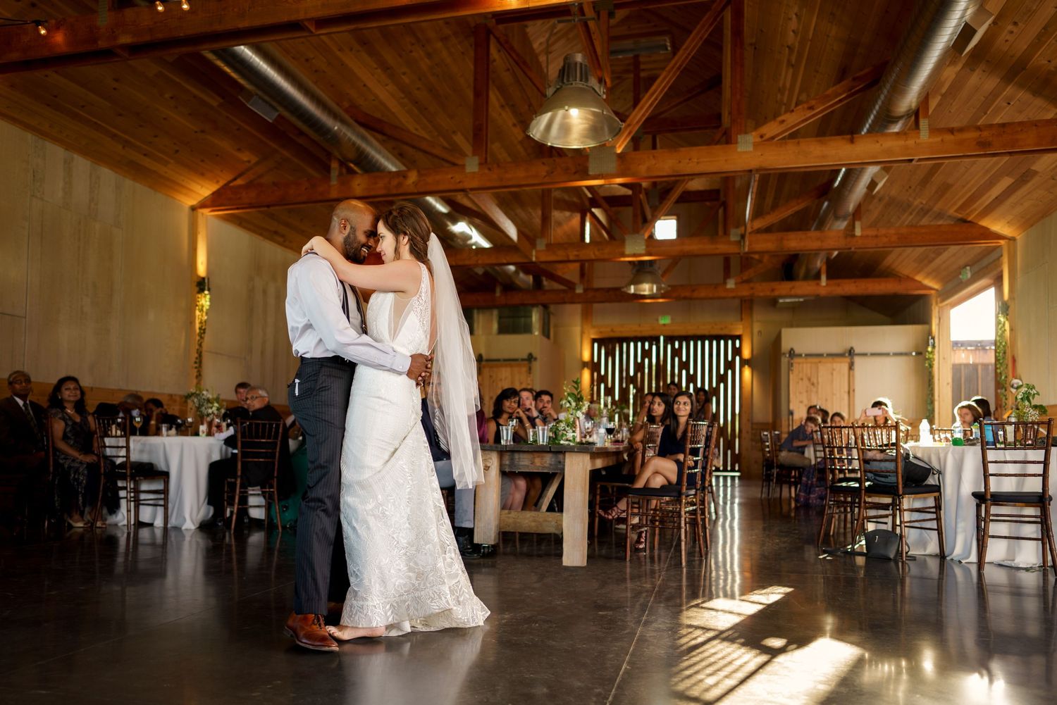 Wedding couple shares intimate dance in rustic wooden beam venue.