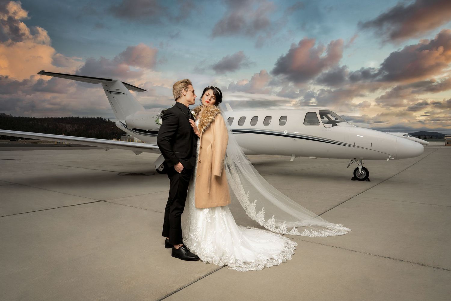 Newlyweds pose together on airport tarmac with private jet at sunset.