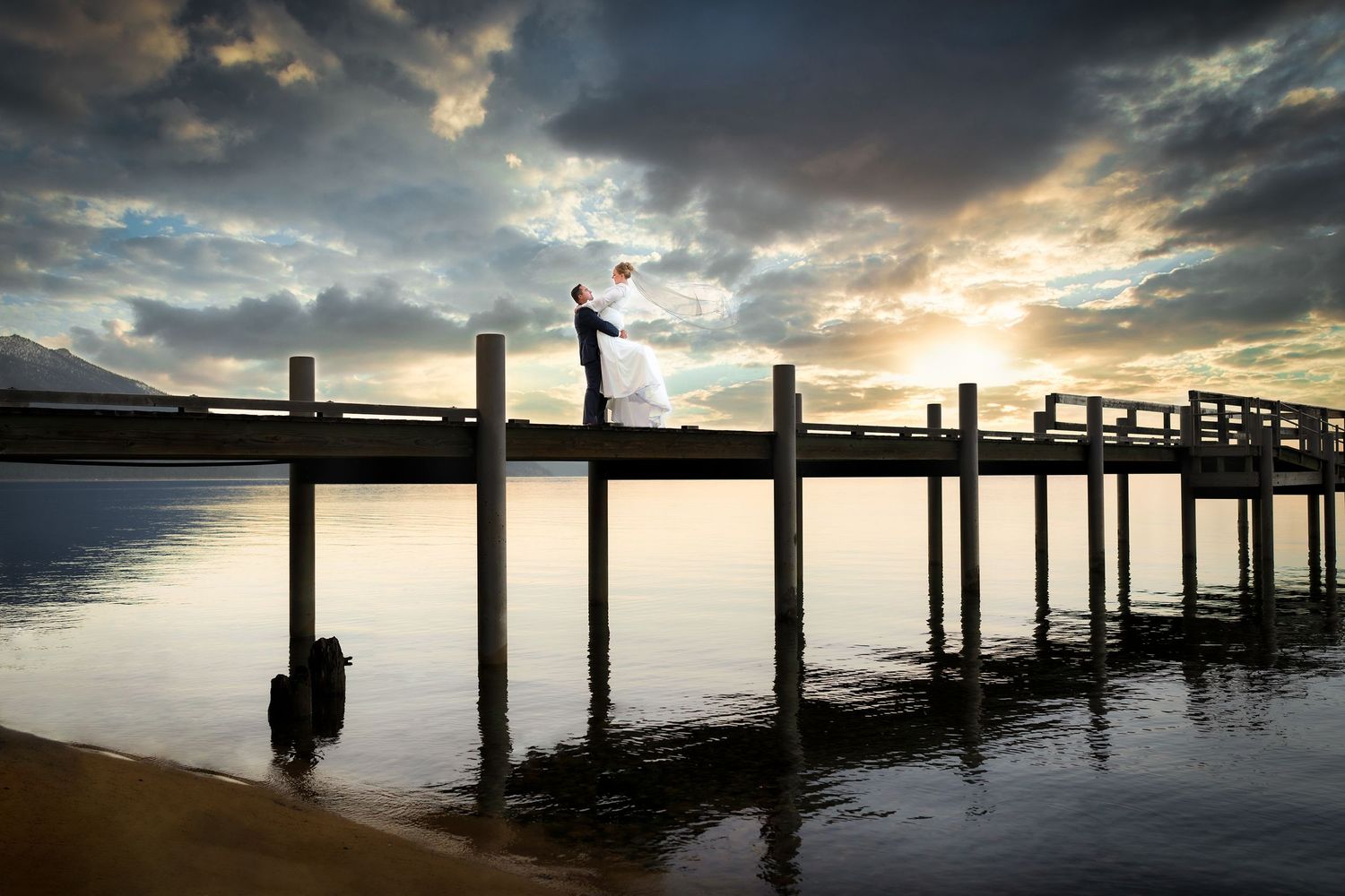 Dramatic sunset over a wooden pier with silhouetted posts reflecting in calm water.