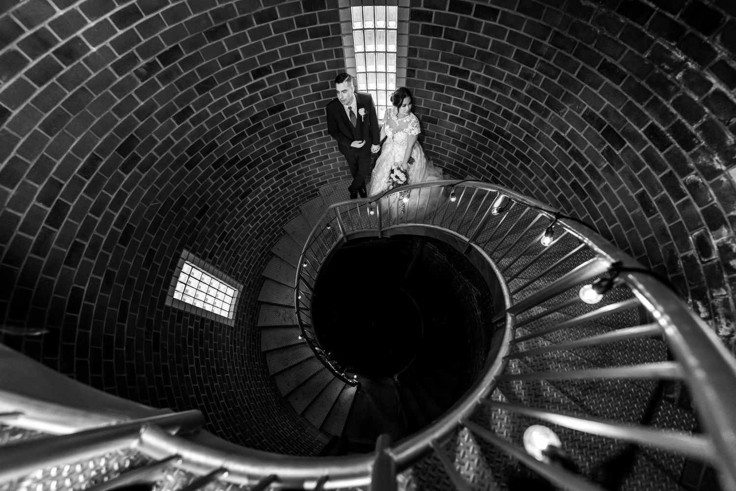 Black and white spiral staircase photo with dramatic architectural lighting and curved brick ceiling.