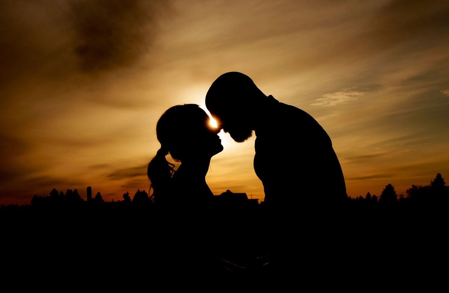 Intimate silhouette portrait against warm golden sunset sky.