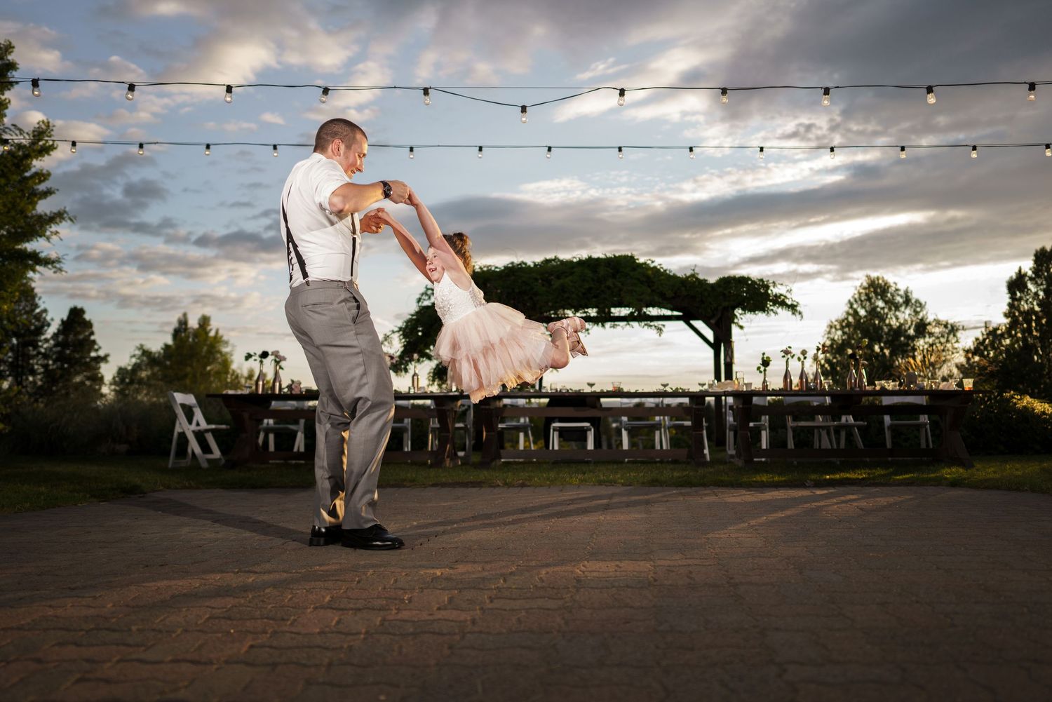 Dynamic wedding photo of couple dancing under string lights at outdoor reception venue.