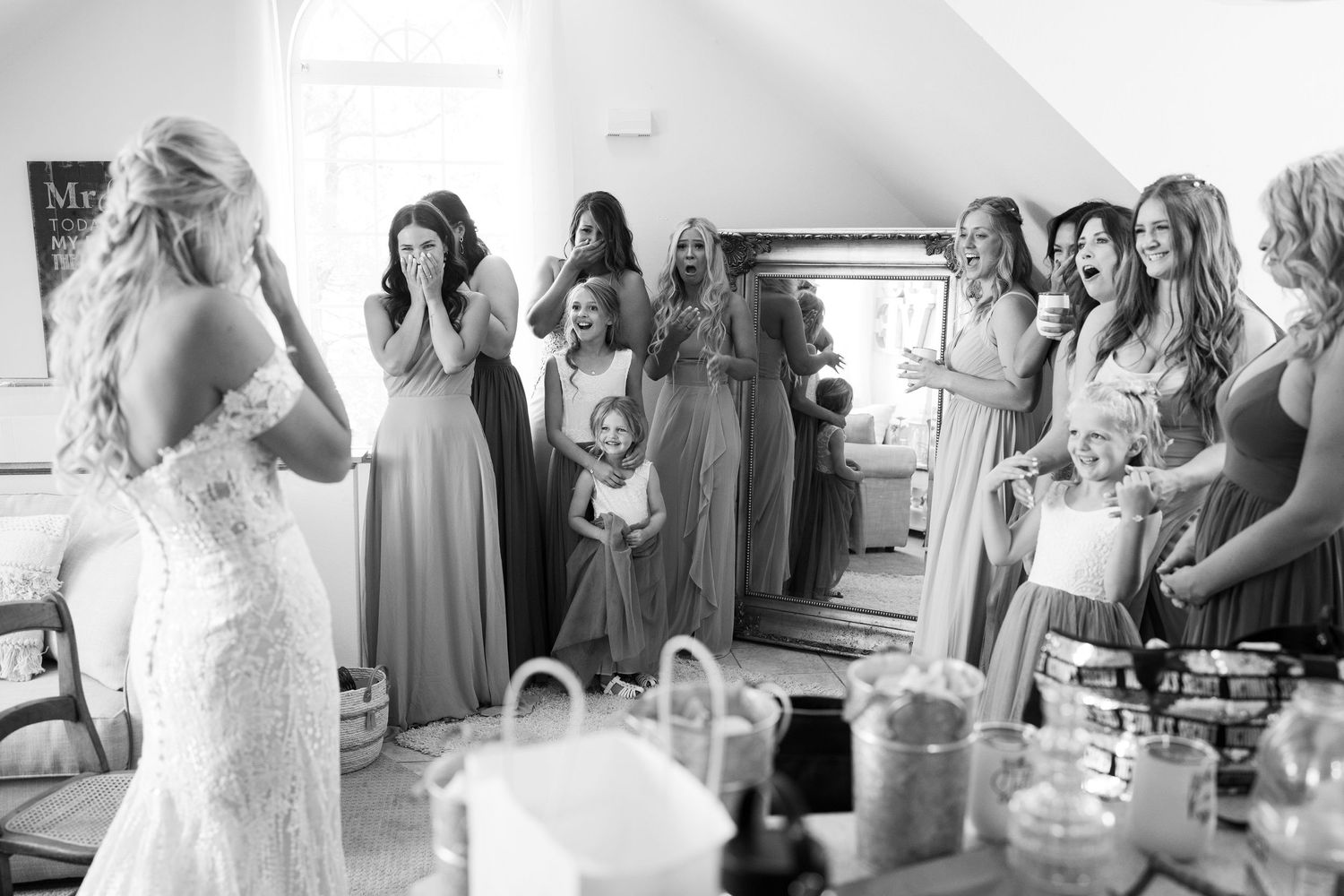 A candid black and white photo of bridesmaids reacting during wedding preparations.