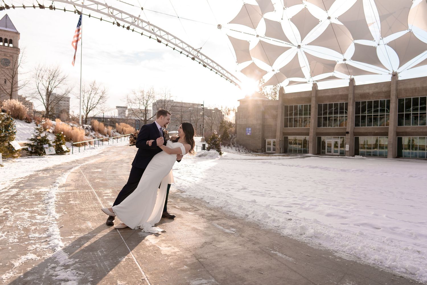 A wedding couple dips dramatically on a snowy path with geometric architecture in the background.