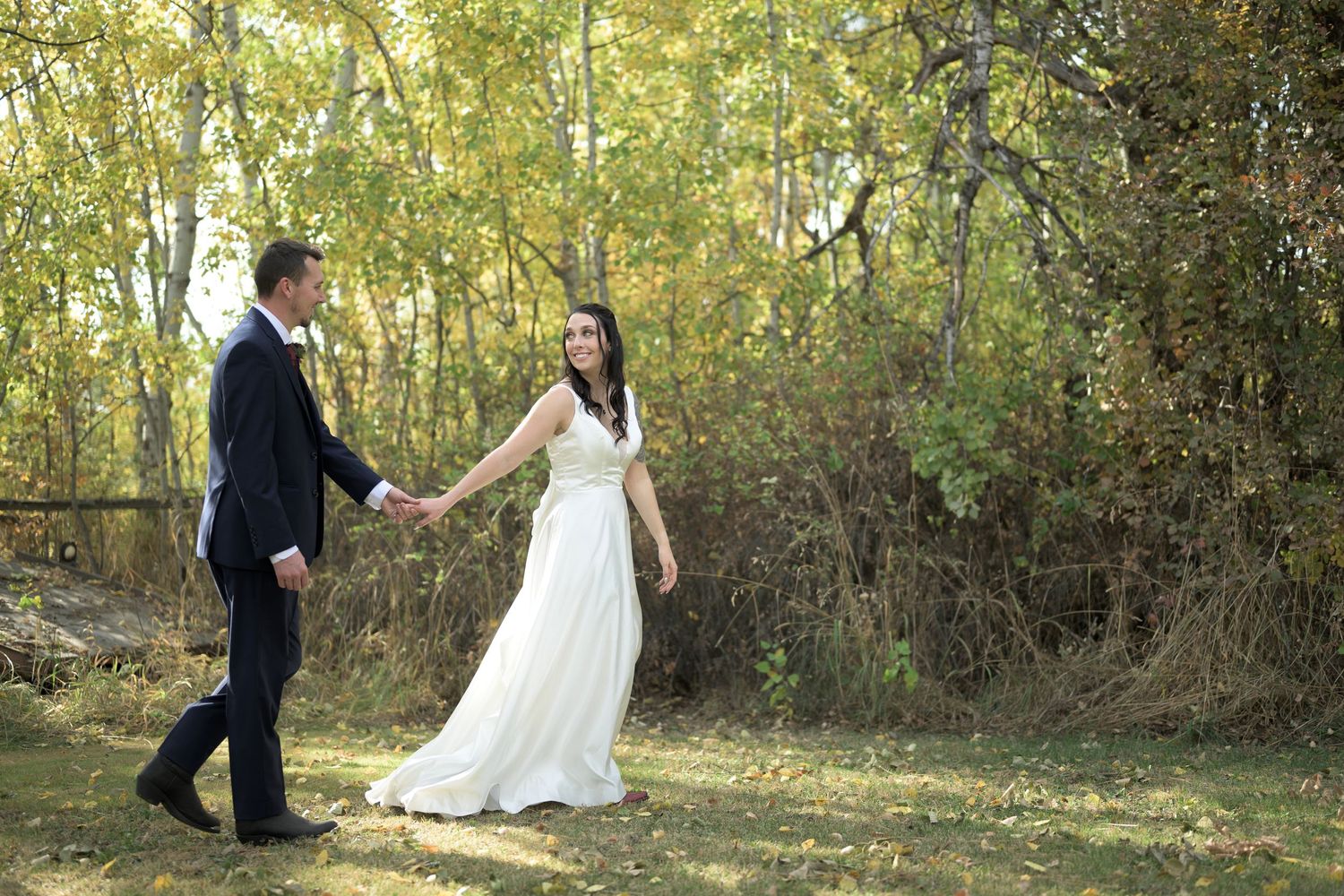 Couple walking hand in hand through autumn foliage in natural outdoor setting.