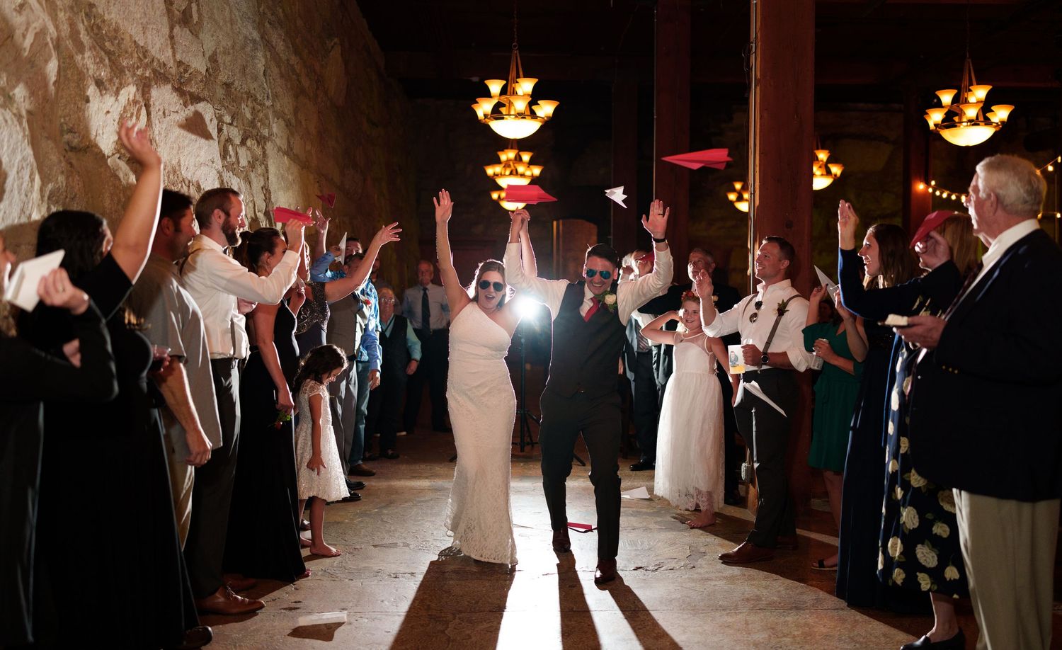 Wedding reception entrance through lined-up guests in a dimly lit stone corridor.