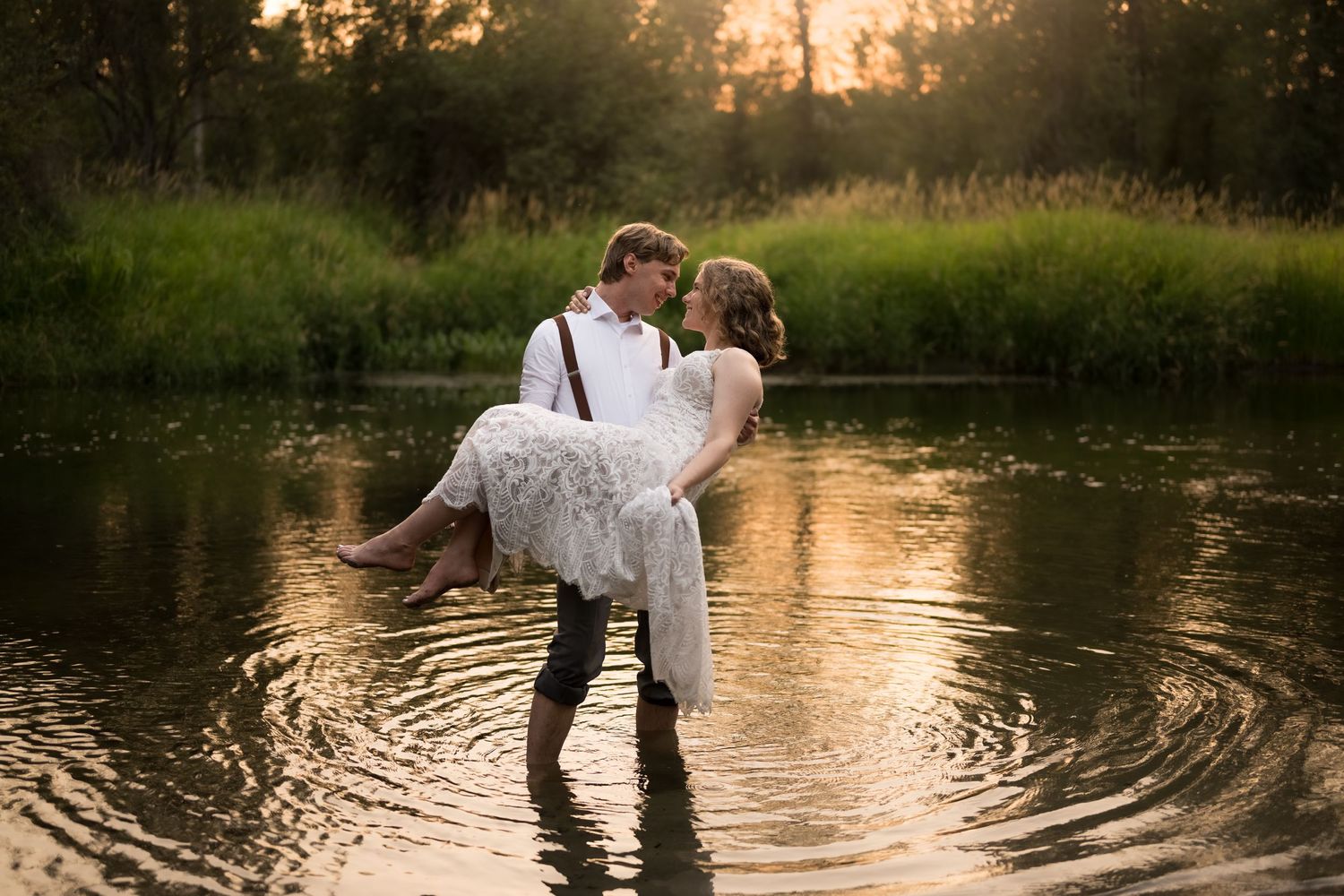 Romantic sunset photo with couple standing in reflective water surrounded by nature.