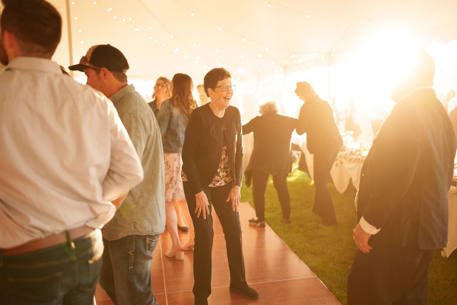 Wedding reception guests mingling and dancing in warm evening light.