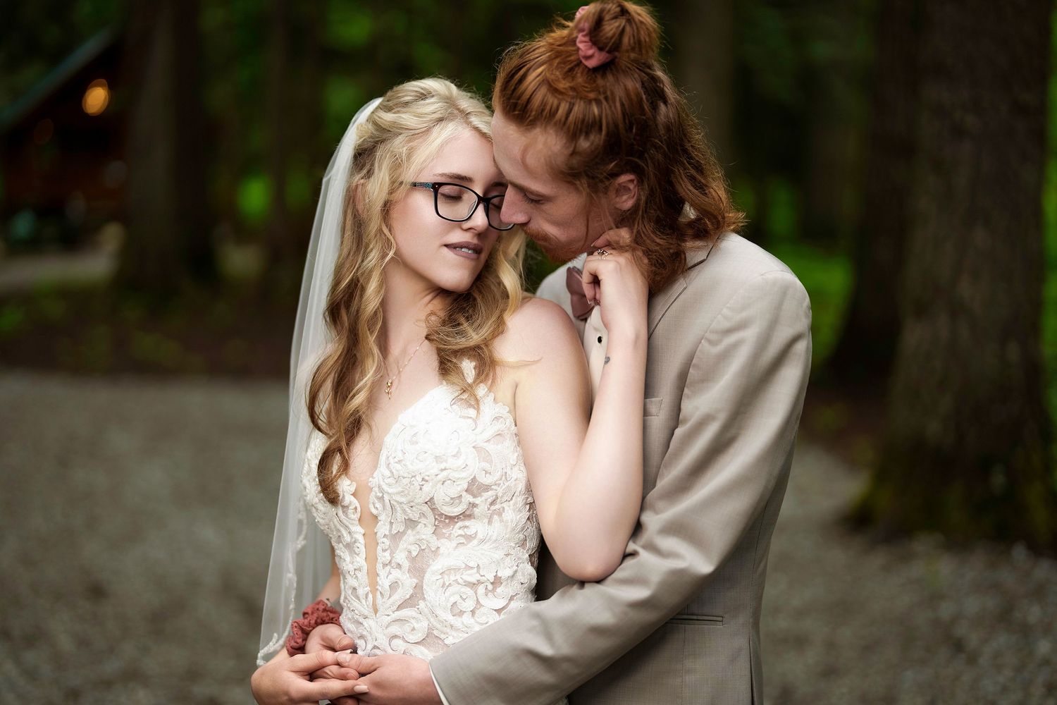 Intimate wedding moment captured as couple embraces in woodland setting wearing formal attire with romantic lighting.