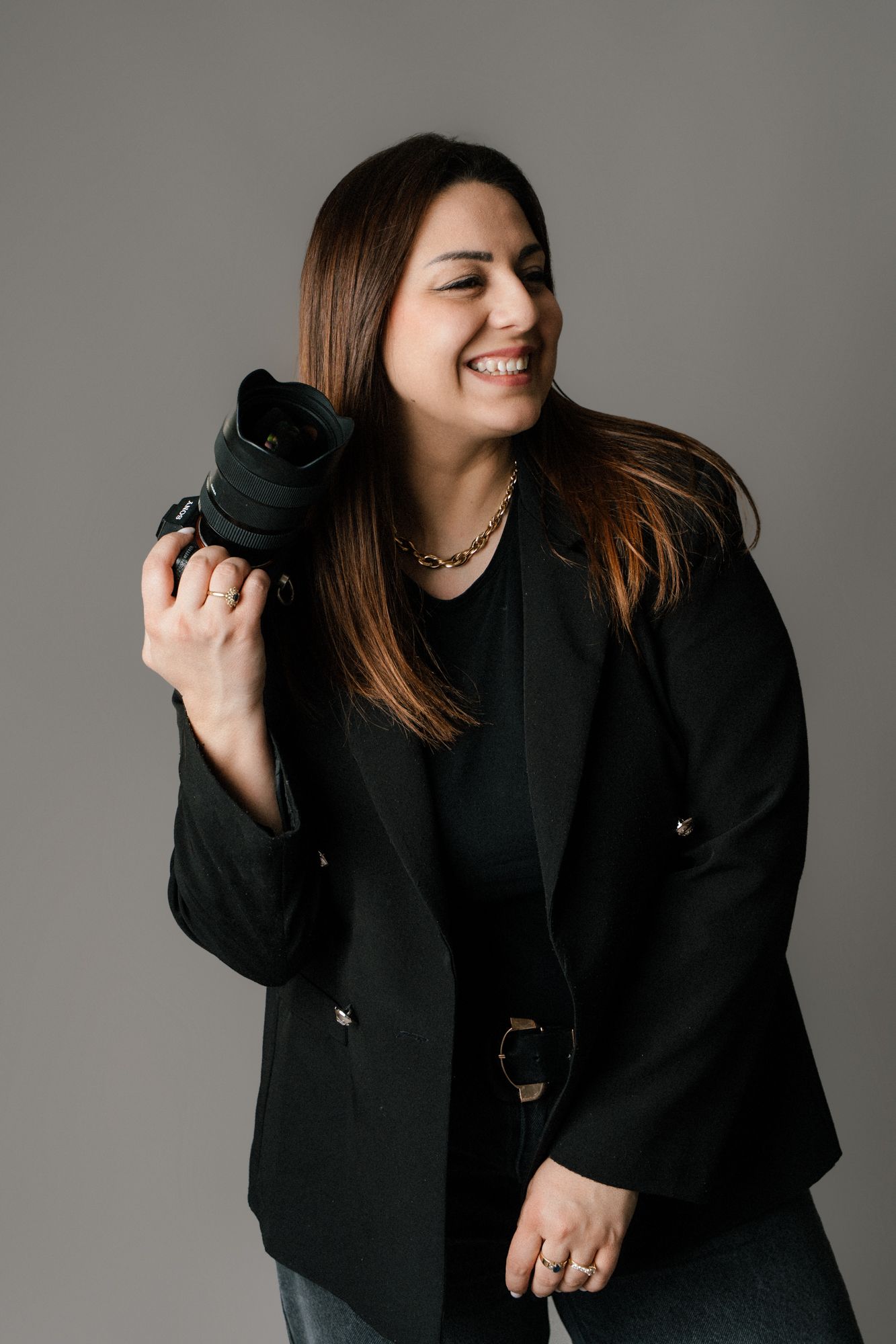 Professional fashion portrait series showing model in black blazer posing playfully against gray studio backdrop.