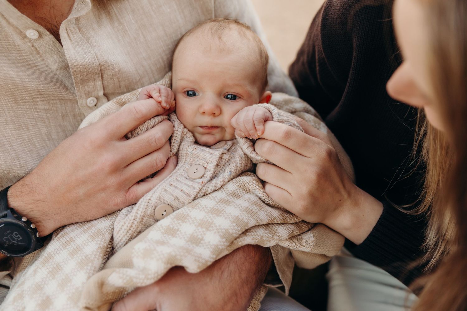 Newborn baby wrapped in a soft blanket being cradled by parents hands in a warm, intimate moment.