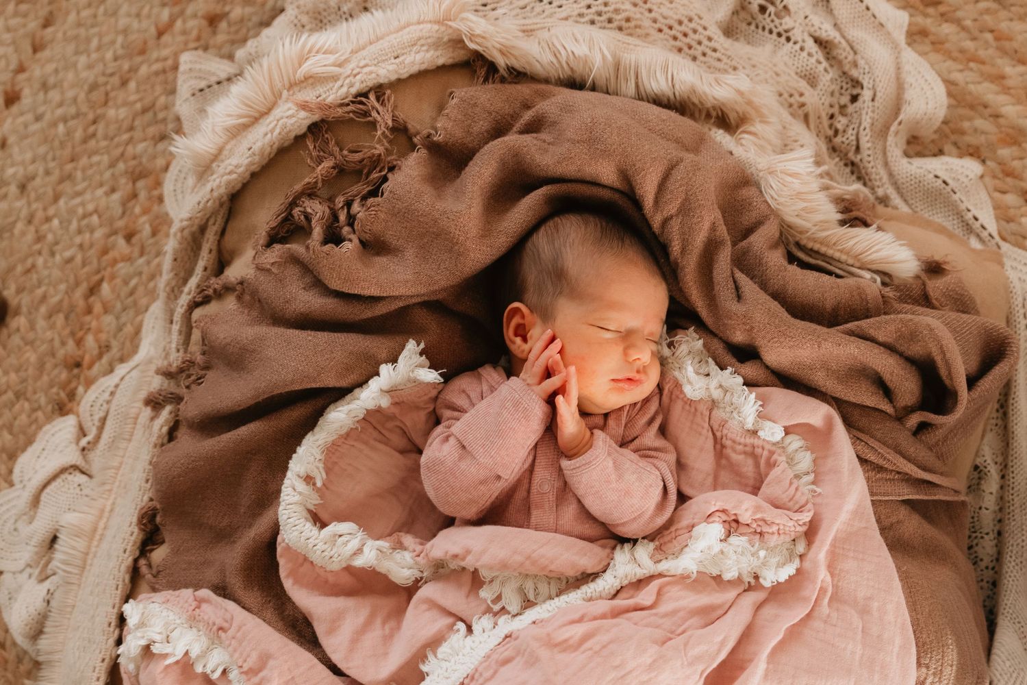 Newborn baby sleeping peacefully wrapped in soft pink blankets during a professional newborn photography session.