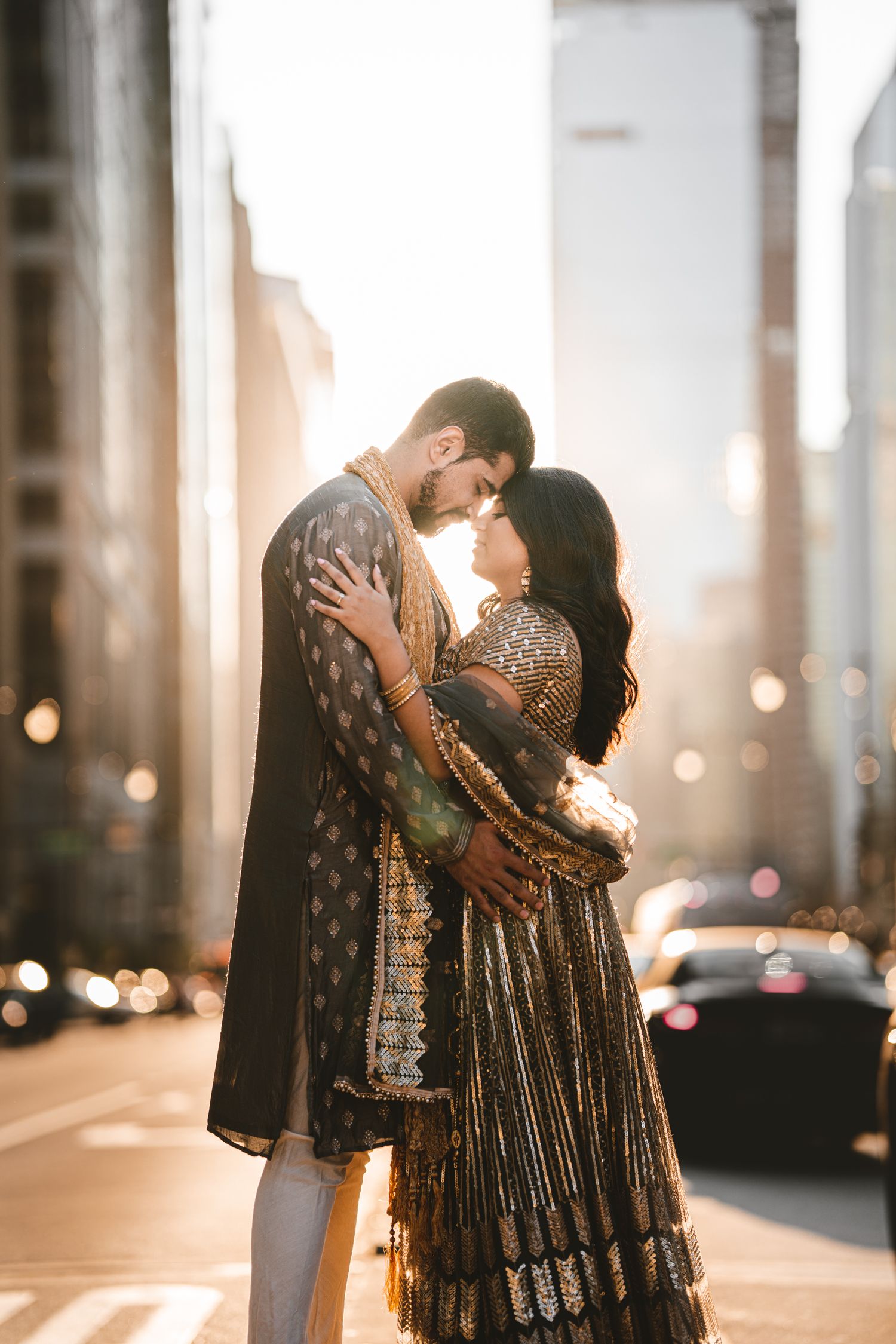 A romantic couple in traditional Indian formal wear embraces on a city street at sunset. Indian Wedding Photography Toronto GTA