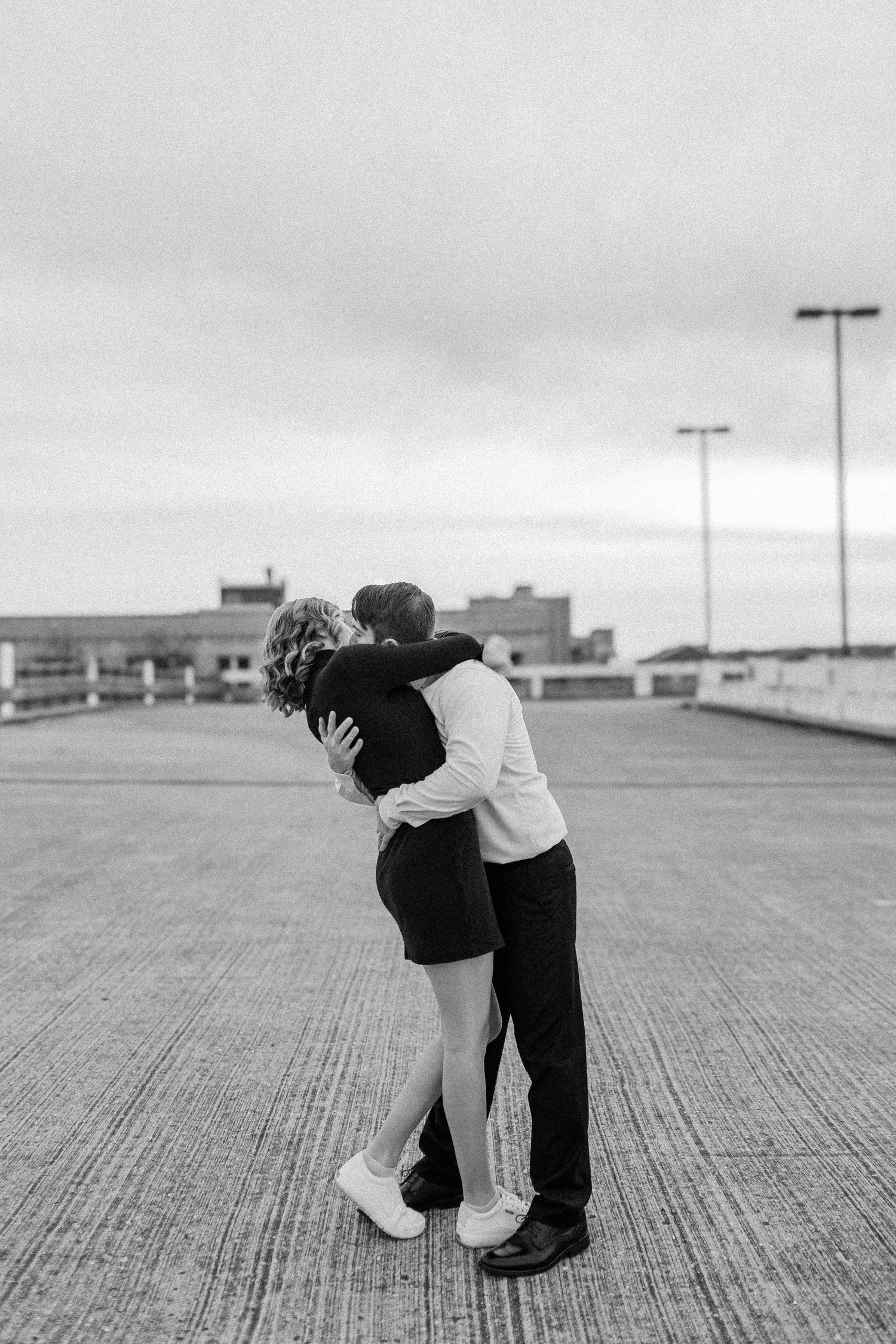 Black and white portrait of couple embracing on empty rooftop parking structure.