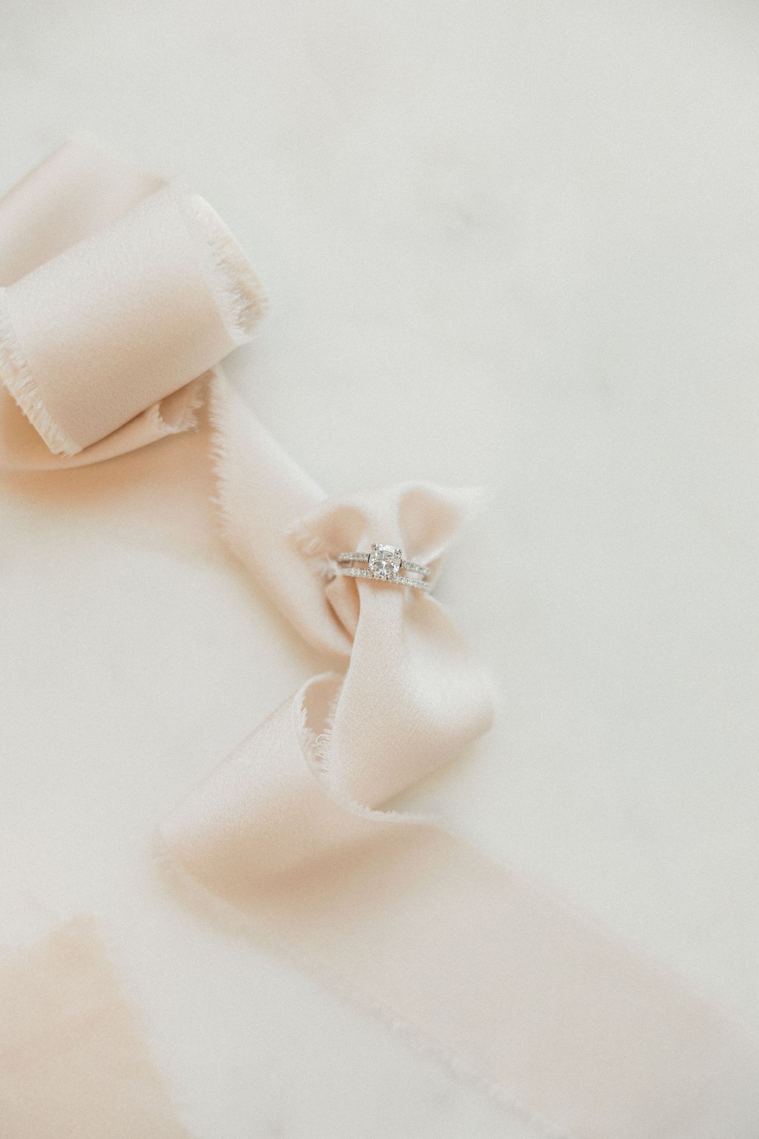 Diamond engagement ring resting on soft blush silk ribbon on marble surface.