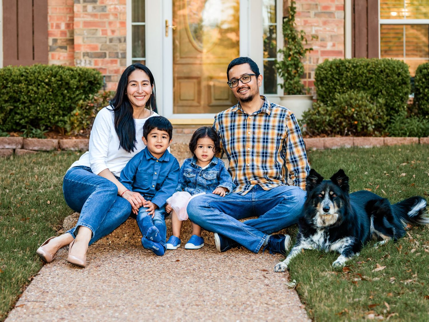 Family wearing matching blue outfits sits together on grass with their black and white border collie dog.