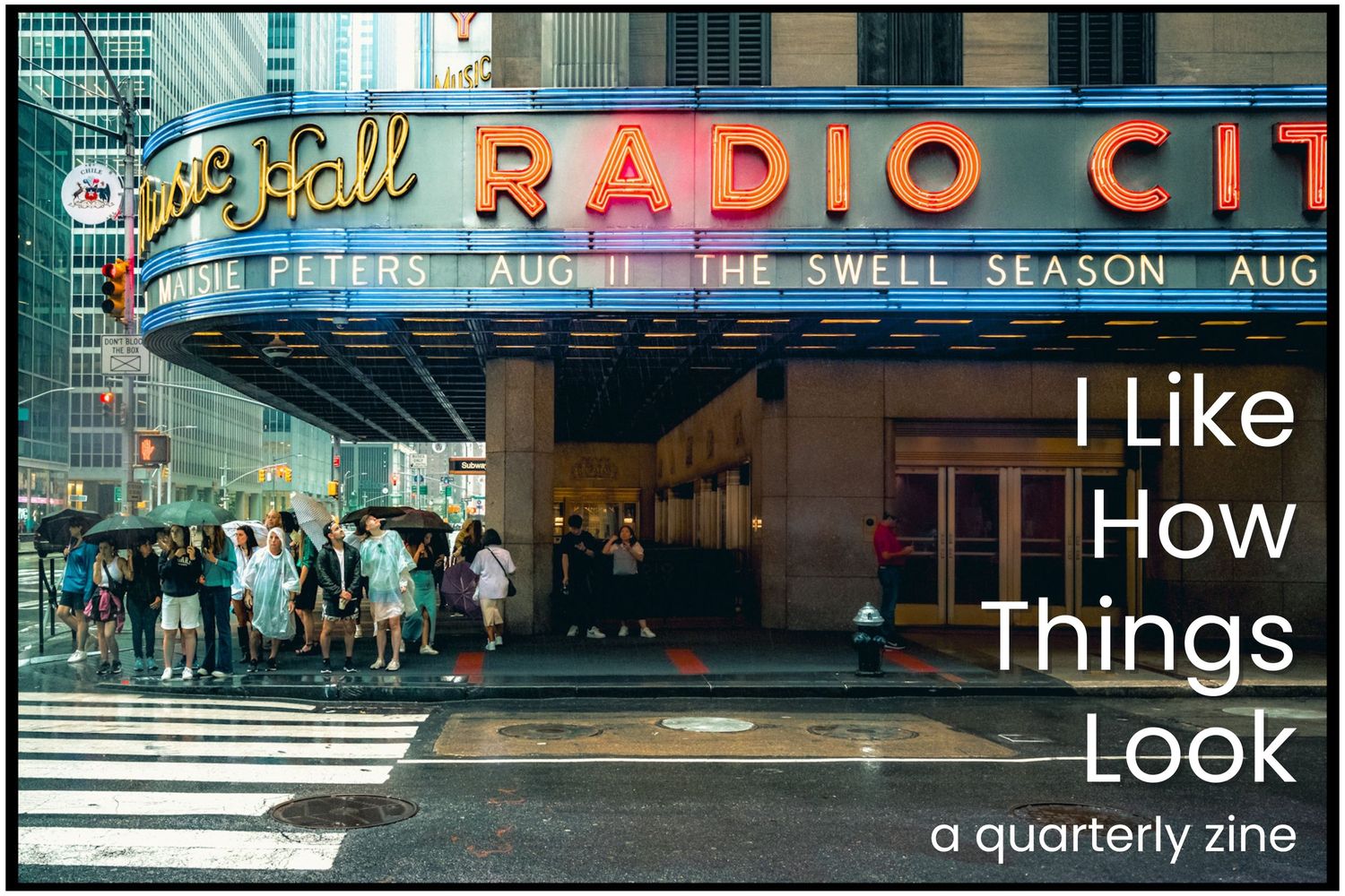 The iconic Radio City Music Hall entrance with neon signage and a line of people waiting outside on a rainy city street.