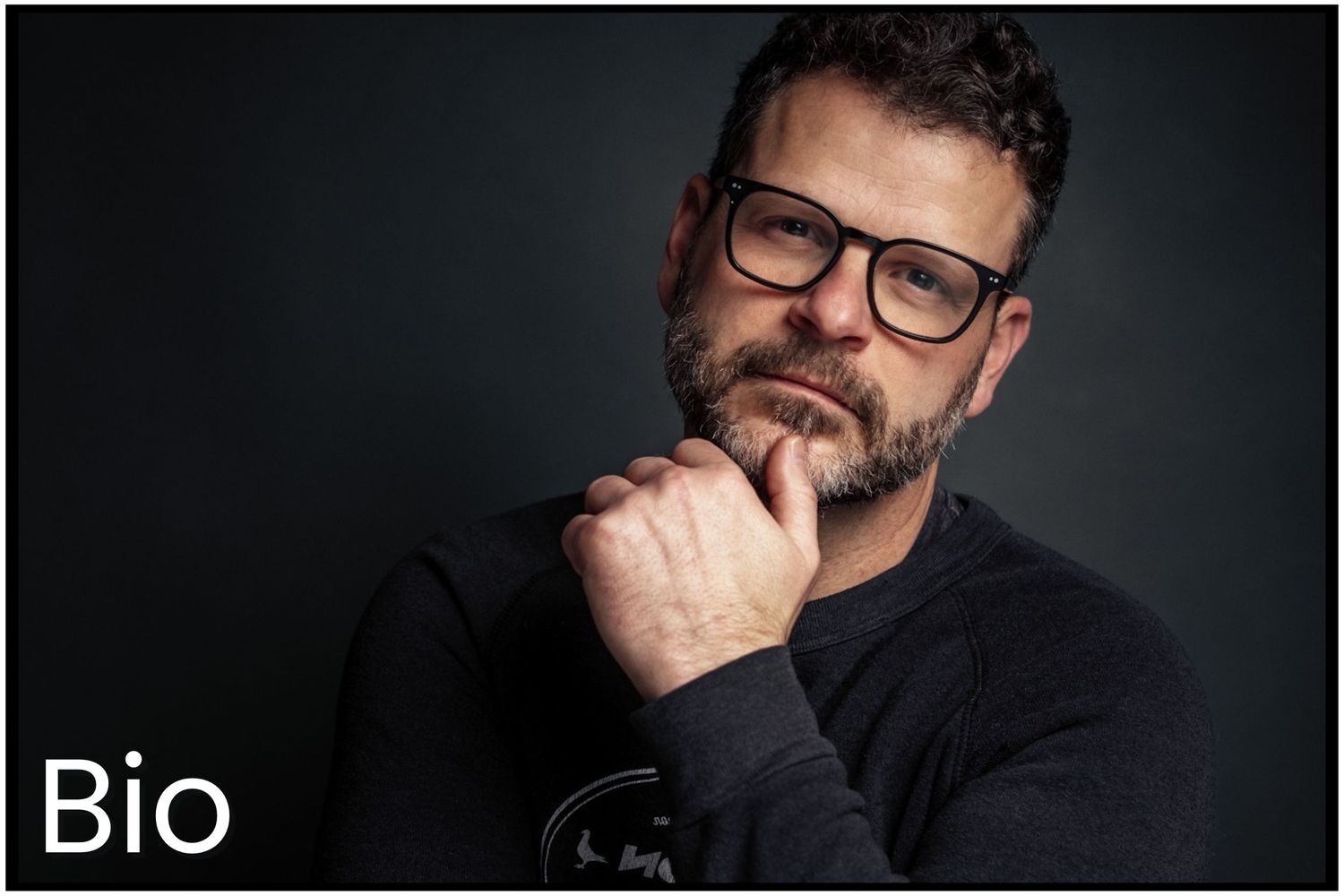A contemplative person in glasses wearing black against a dark background with Bio text overlay.
