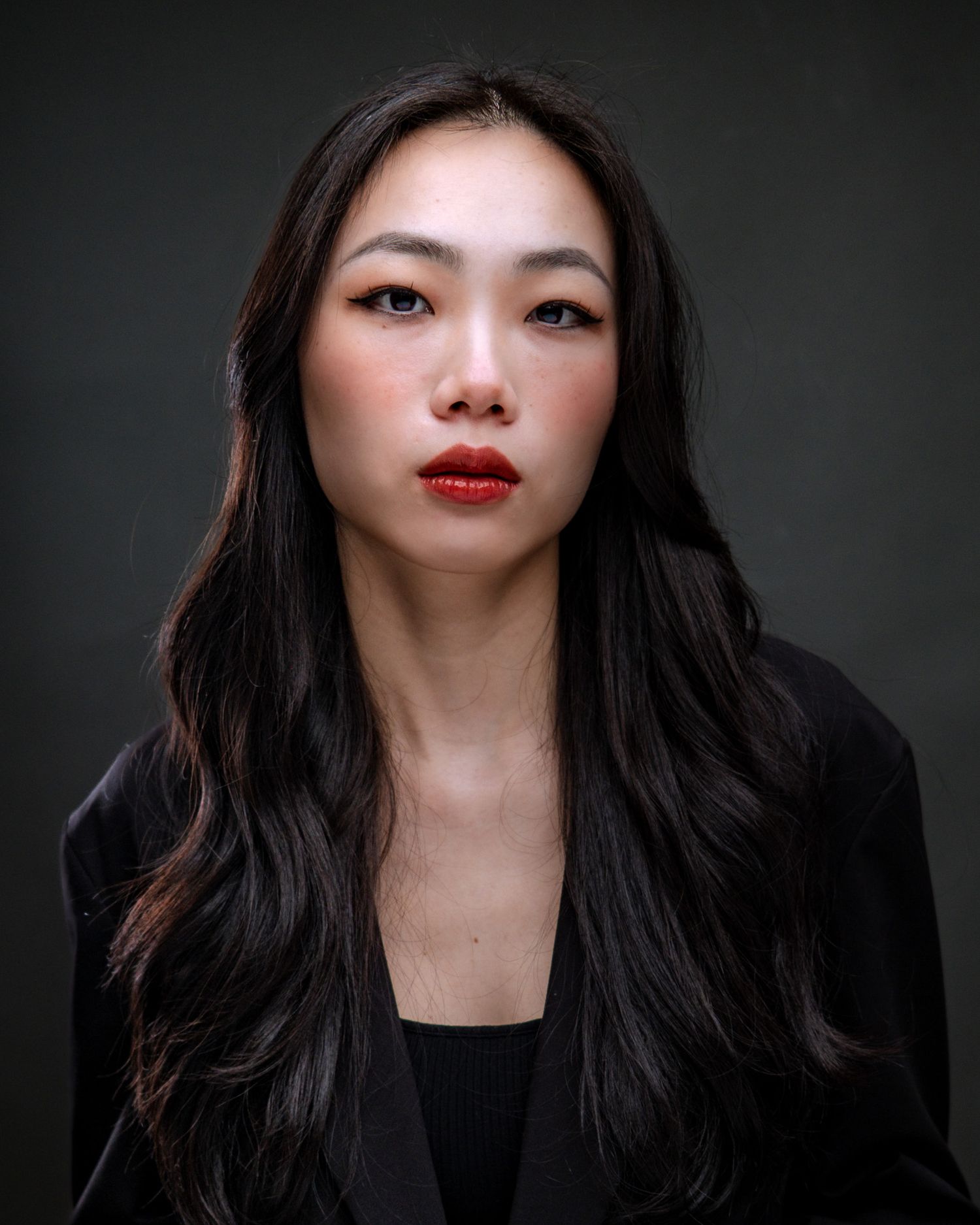 Portrait against dark background featuring long black hair, red lipstick and black top creating dramatic contrast.