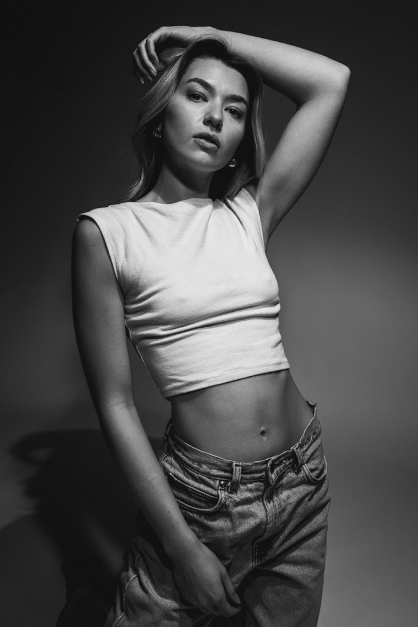 Black and white fashion portrait of a model in a cropped white top and high-waisted jeans striking a dramatic pose.