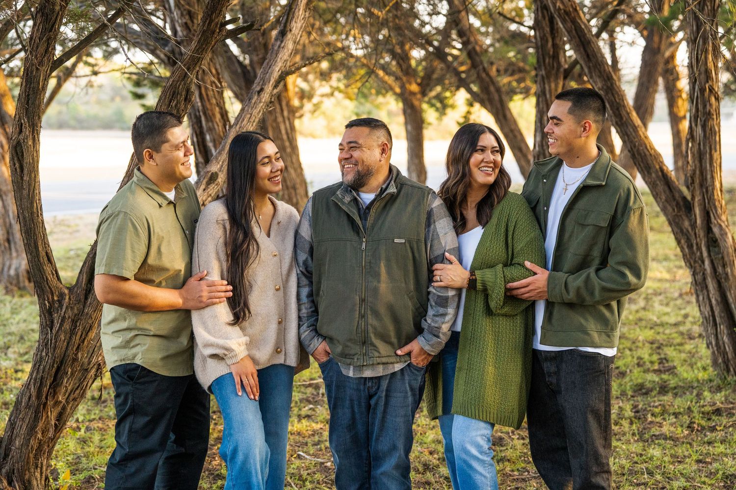 A joyful family of five poses outdoors among trees in a park during golden hour fall season.