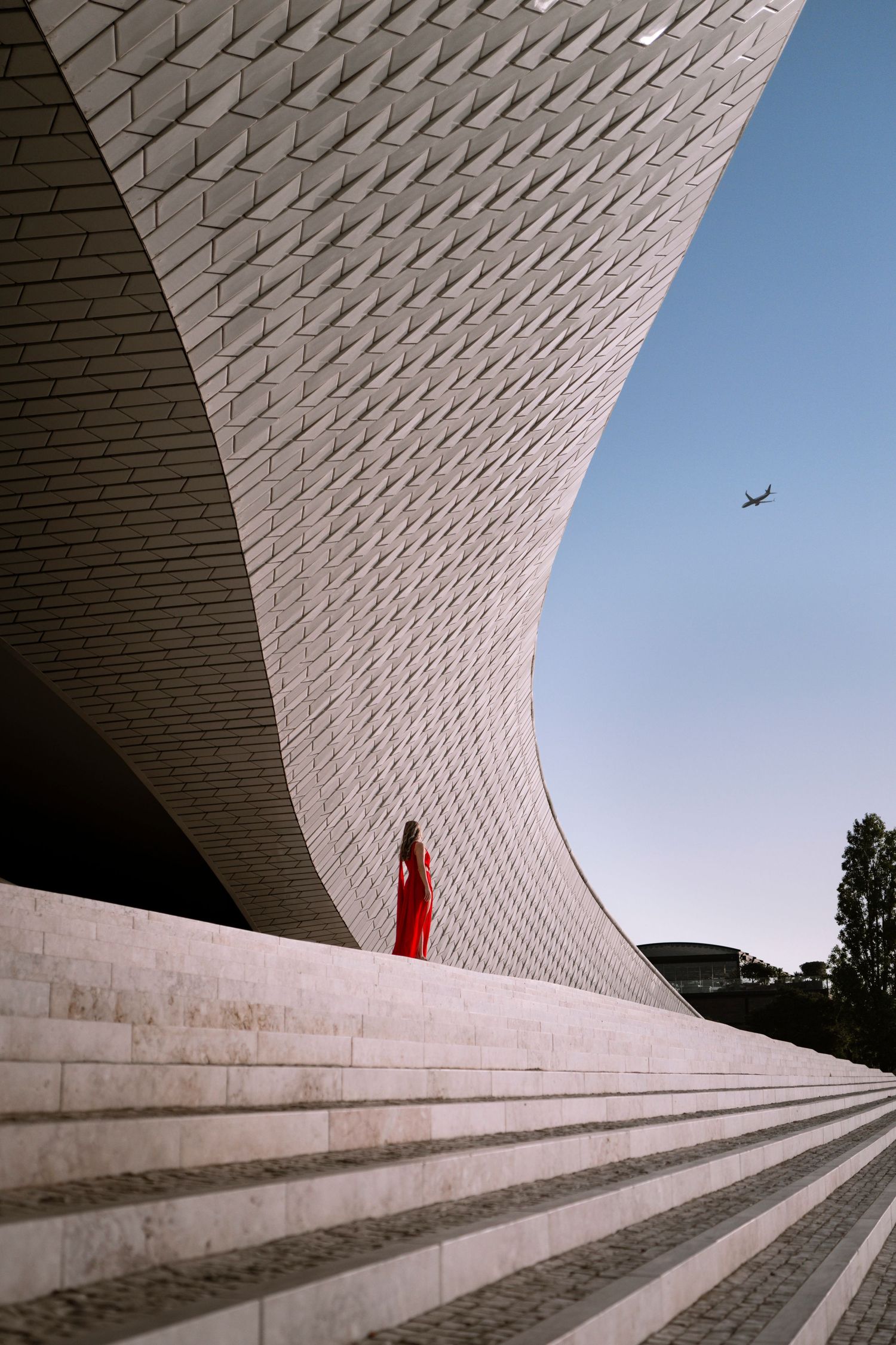 Modern architectural detail of white curved building with geometric steps and red accent against blue sky.