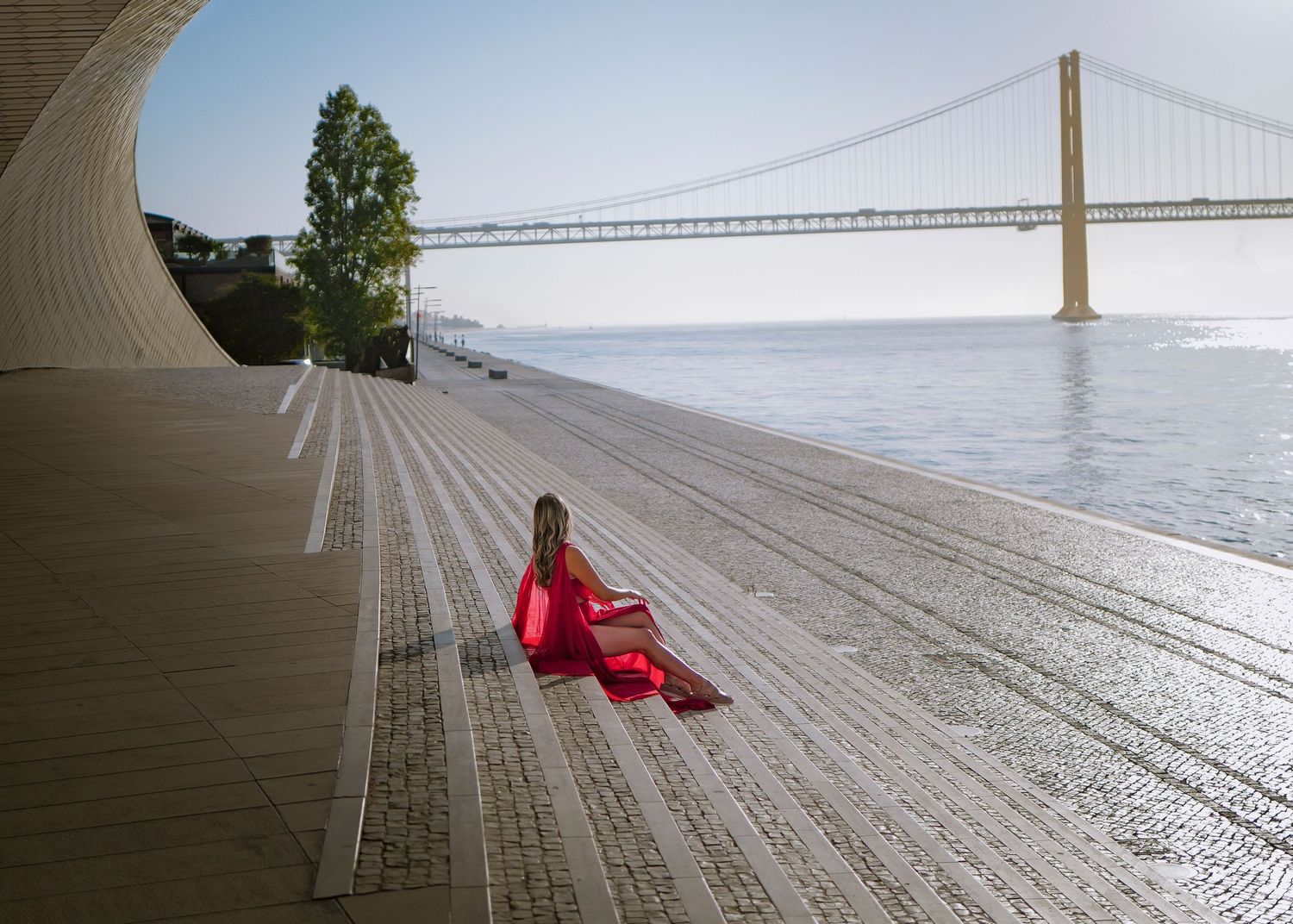 Minimalist wooden deck with red accents overlooking water and bridge in the distance.
