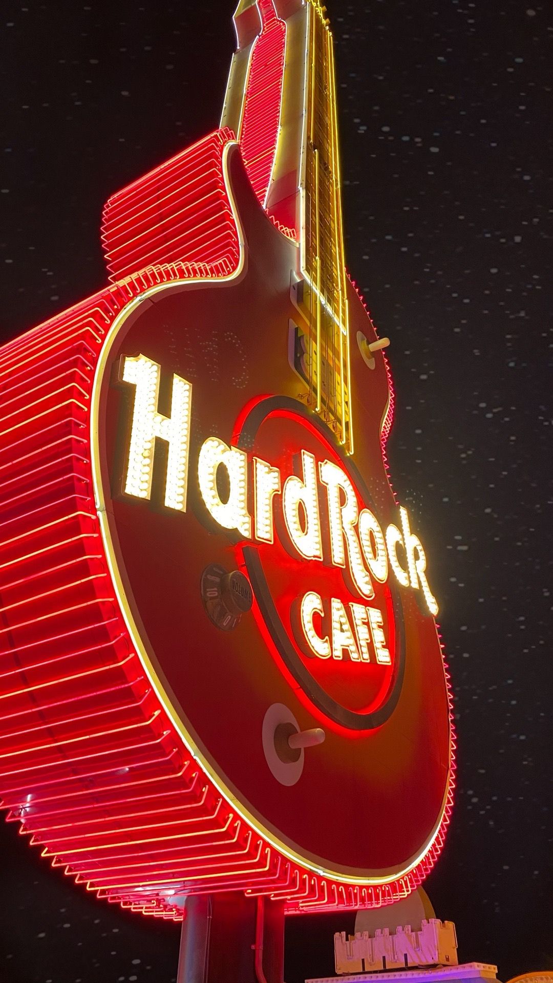 Large red neon Hard Rock Cafe guitar sign glowing against dark night sky.