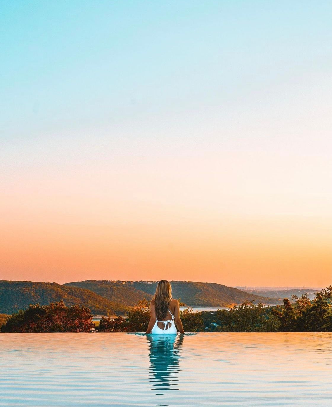Infinity pool overlooking mountains during a colorful sunset.