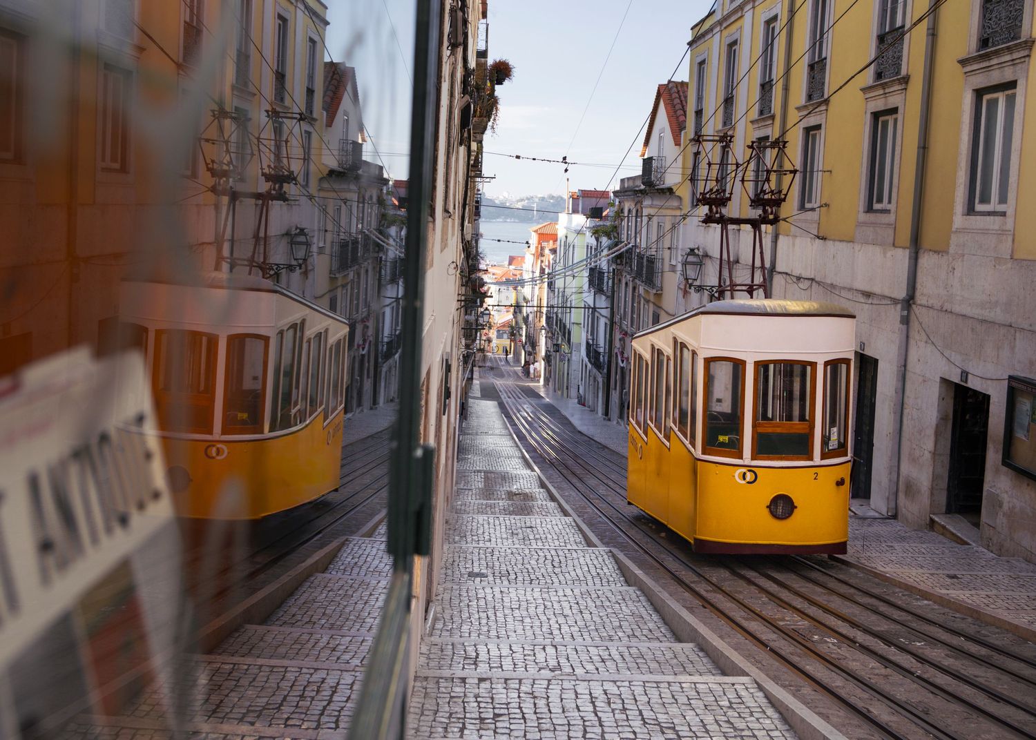 Yellow vintage tram moving through narrow cobblestone streets of Lisbon.
