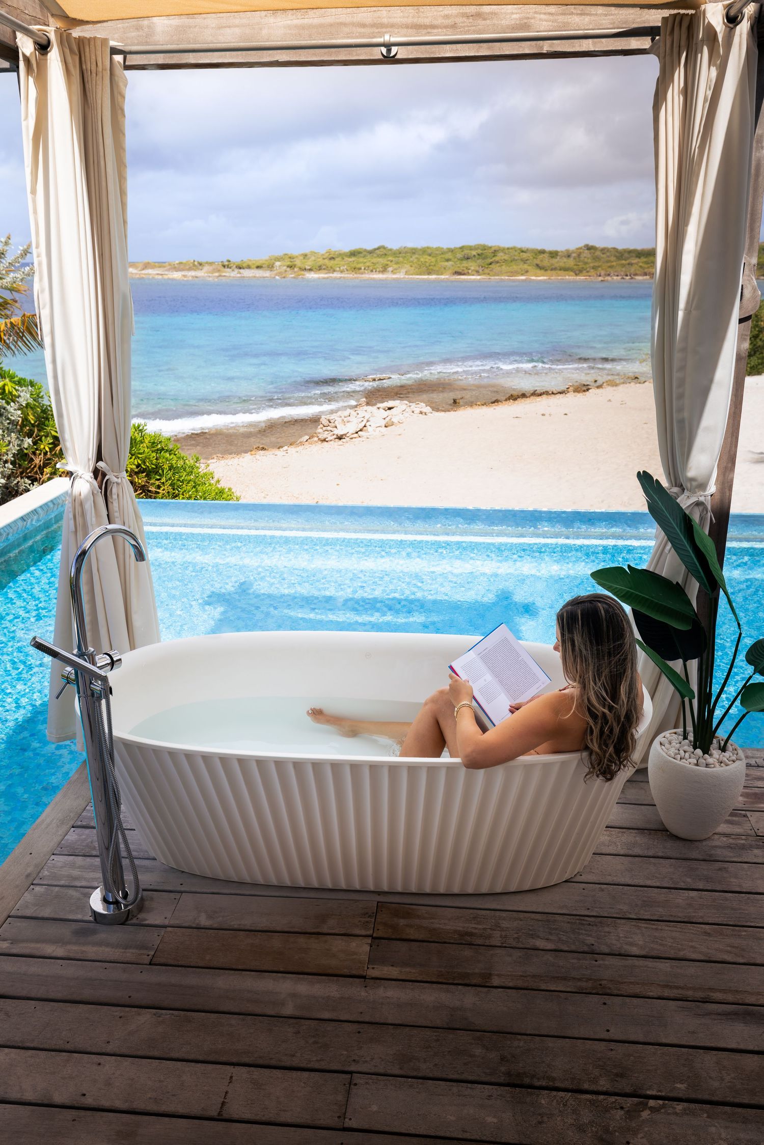 Luxurious beachfront cabana with white curtains overlooking turquoise ocean waters.