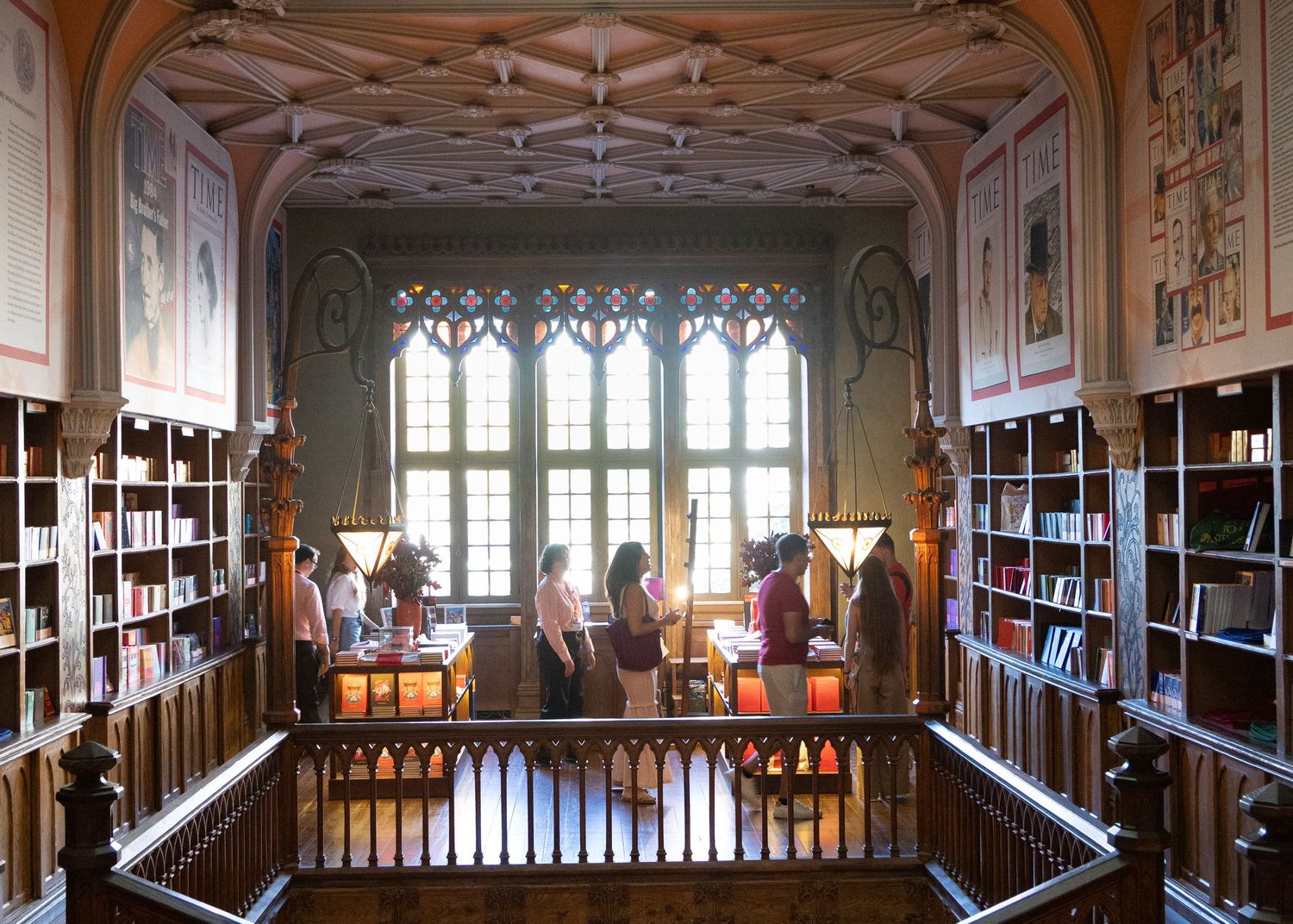 Panoramic view of a grand library interior with wooden shelves and Gothic windows.