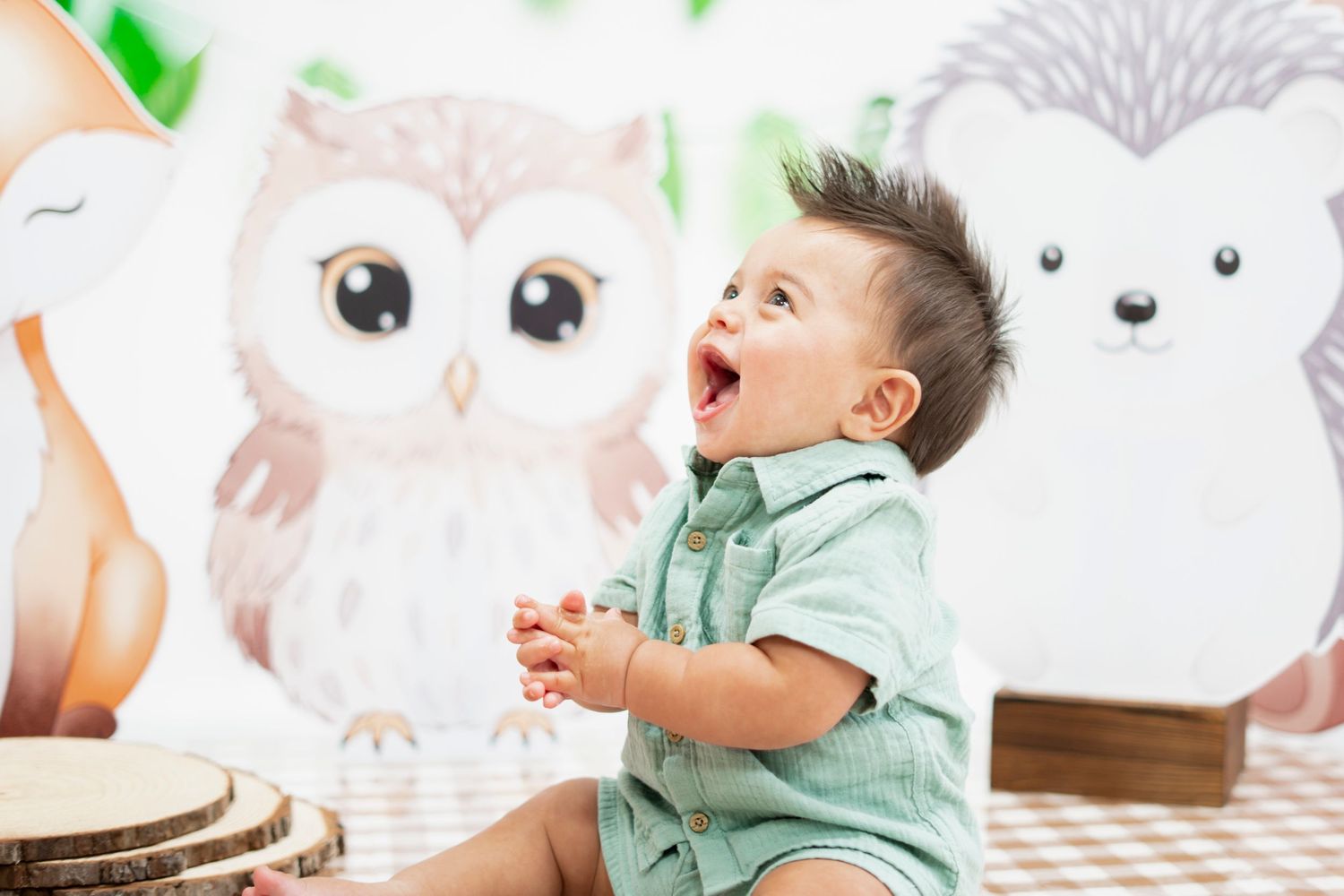 Joyful baby boy laughing at woodland animal themed first birthday party with owl and hedgehog decorations.