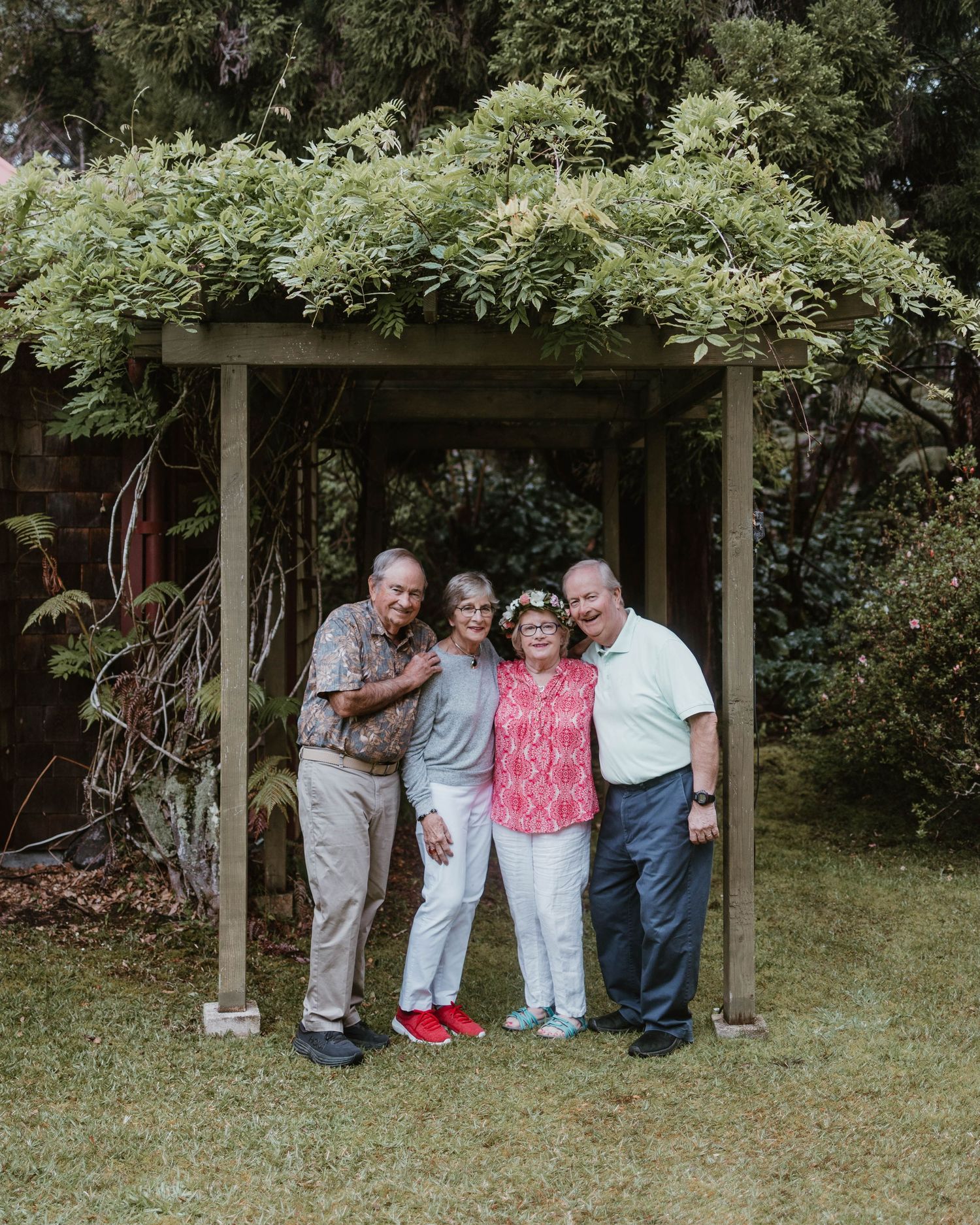 Four people pose under a vine-covered garden pergola for a casual outdoor photo.
